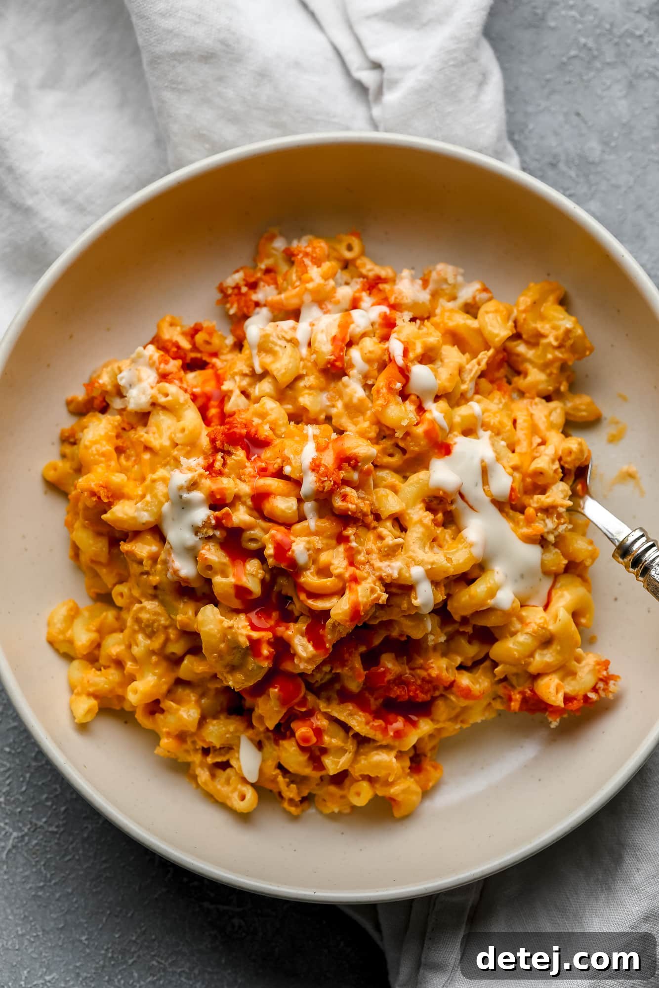 Creamy Vegan Buffalo Mac and Cheeze 2 Vegan Buffalo Mac and Cheese topped with white vegan ranch and hot sauce in a beige bowl.