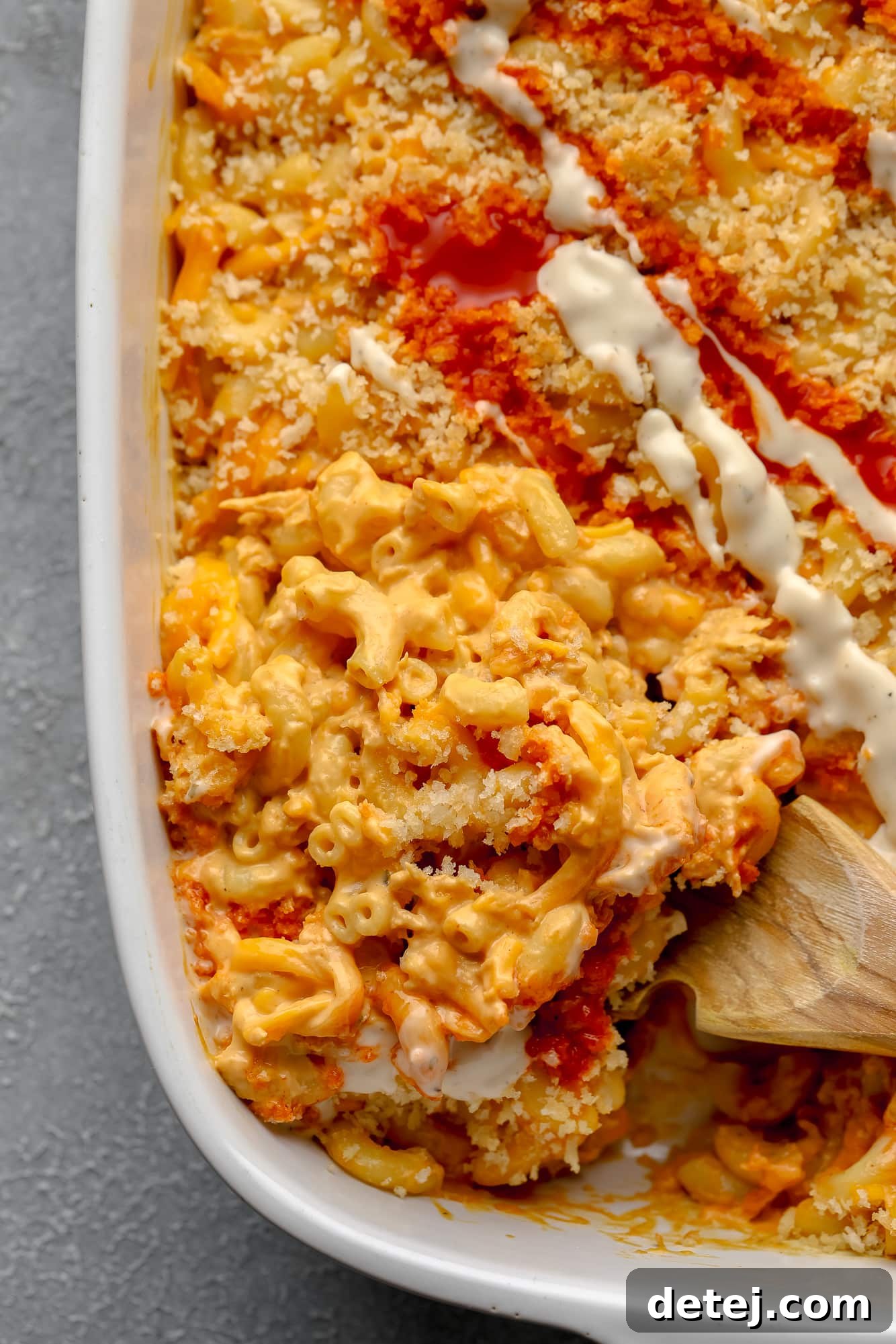 Creamy Vegan Buffalo Mac and Cheeze 3 using a wooden spoon to remove a scoop of Vegan Buffalo Mac and Cheese from a large white casserole dish.