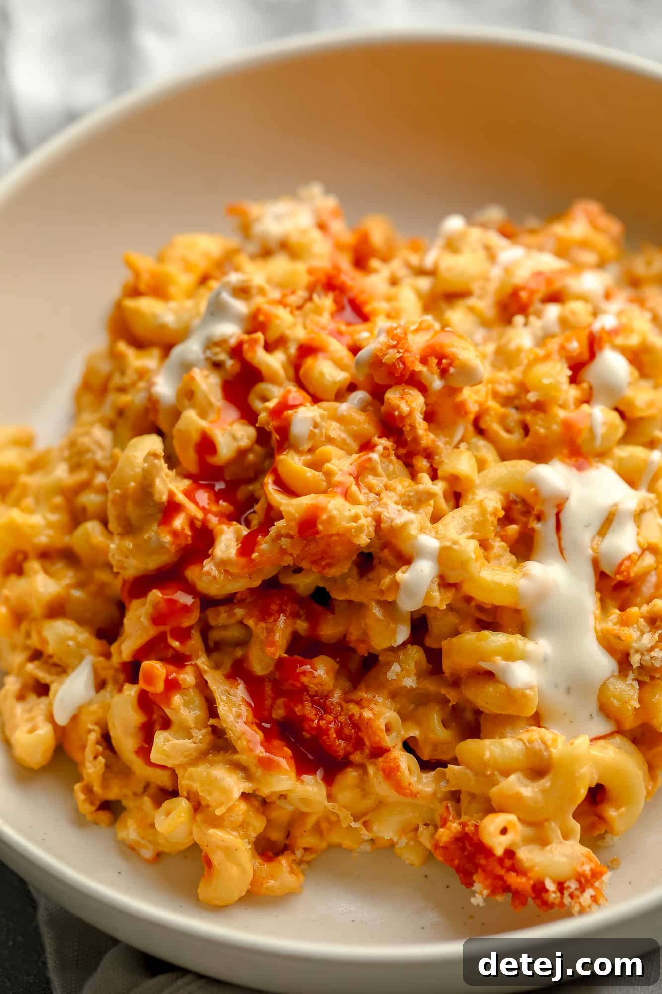 Creamy Vegan Buffalo Mac and Cheeze 7 close up on Vegan Buffalo Mac and Cheese topped with white vegan ranch and hot sauce in a beige bowl.