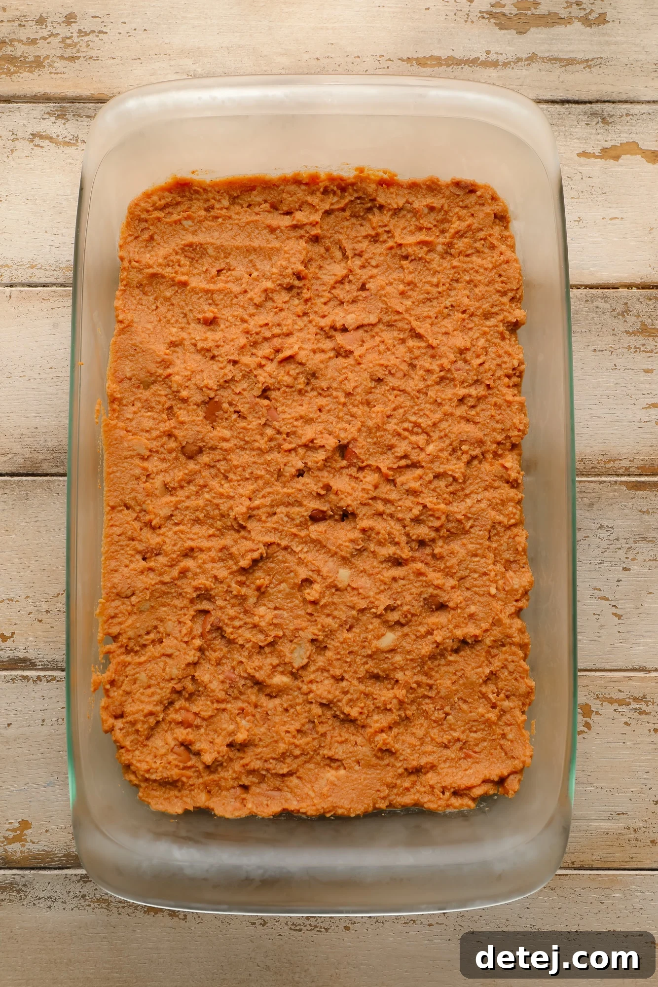 refried beans spread on the bottom of a glass casserole dish.