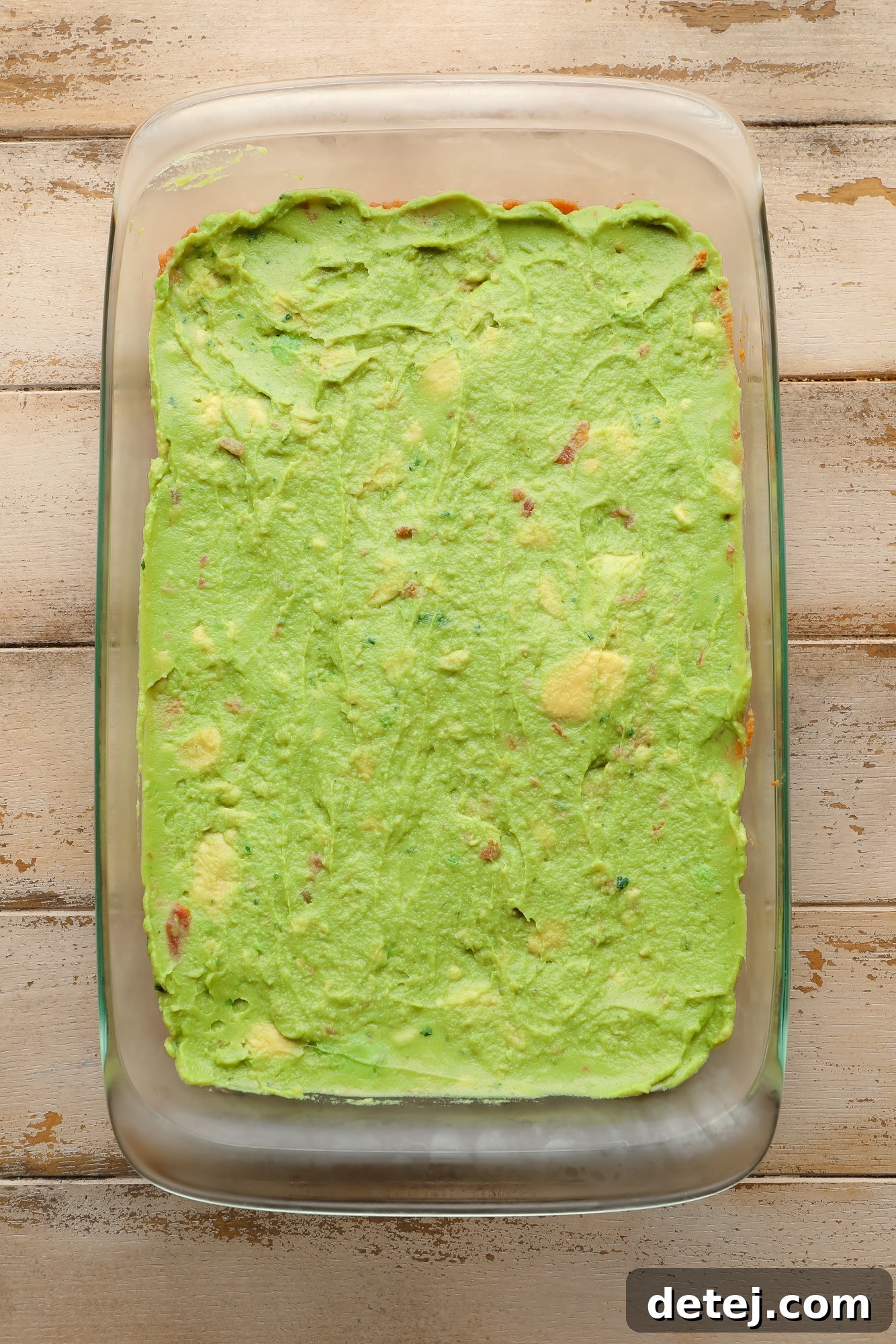 guacamole spread on top of refried beans in a glass casserole dish.