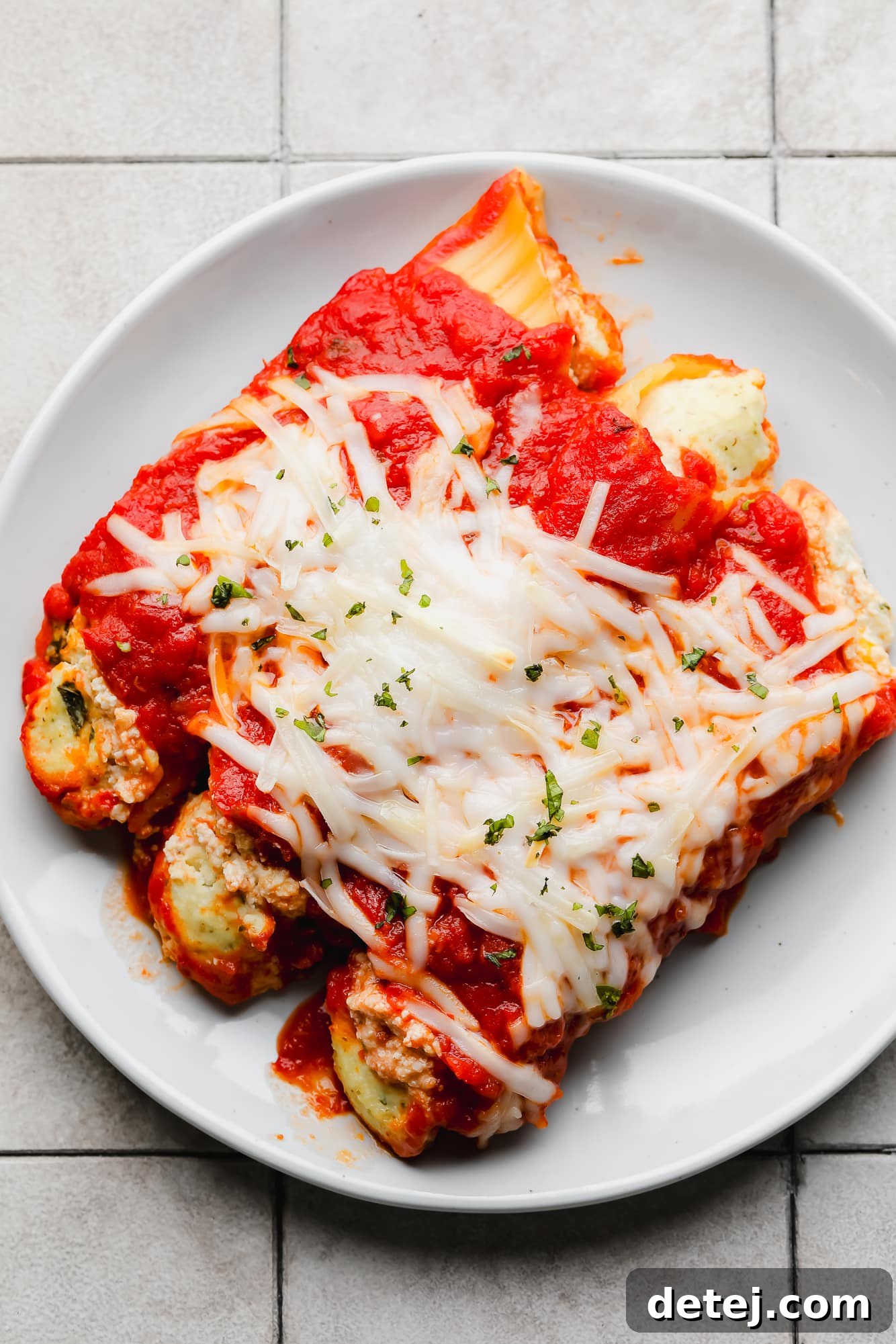 Plant-Based Manicotti 3 3 baked vegan manicotti shells topped with vegan mozzarella on a white plate.