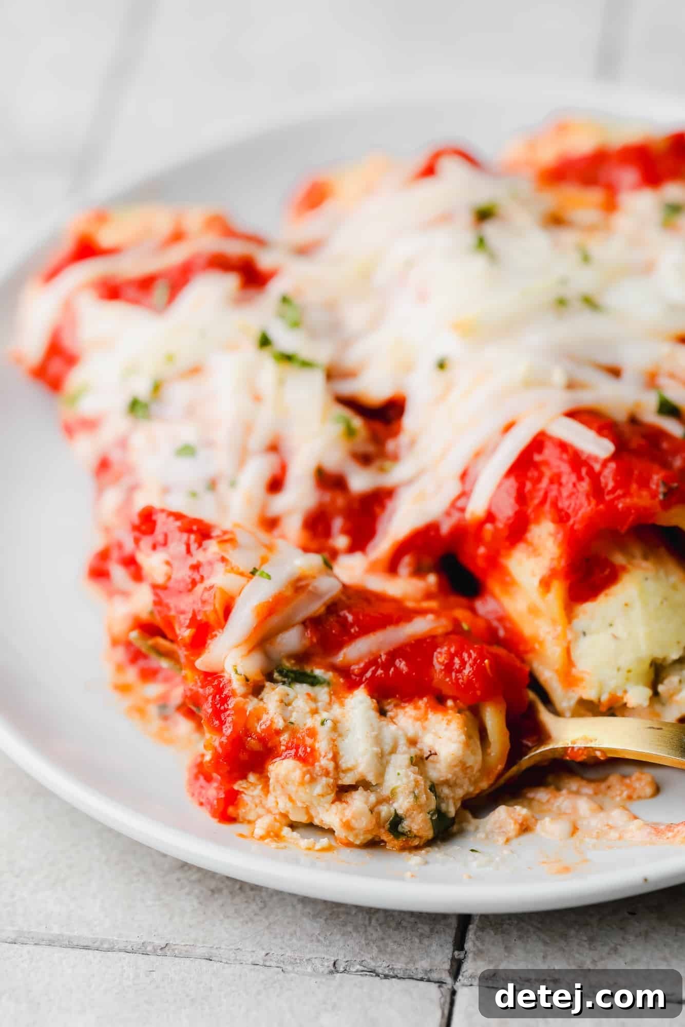 Plant-Based Manicotti 6 close up on a fork taking a scoop of vegan manicotti from a serving on a white plate.