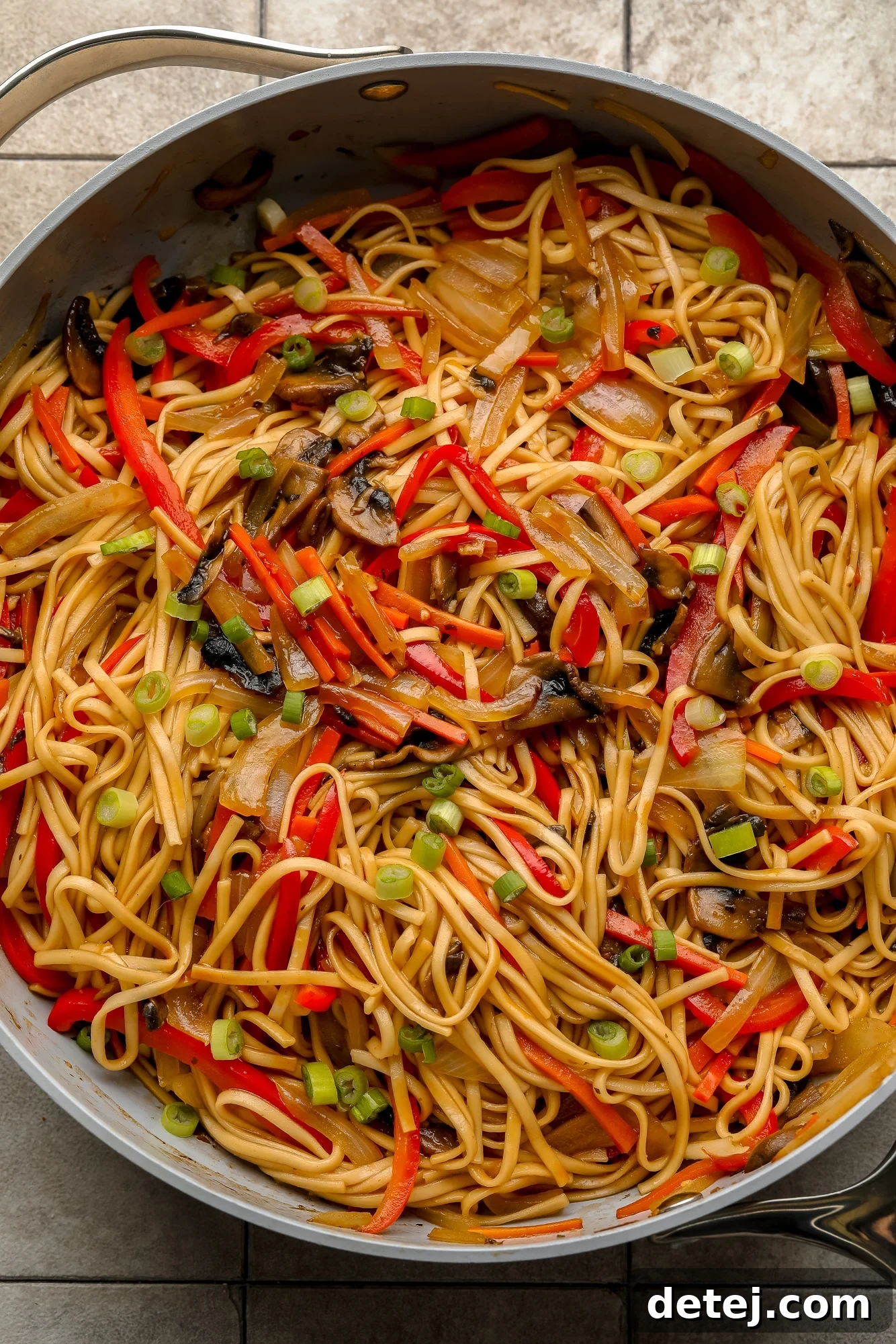 A large gray skillet filled with vibrant vegan lo mein noodles and stir-fried vegetables.