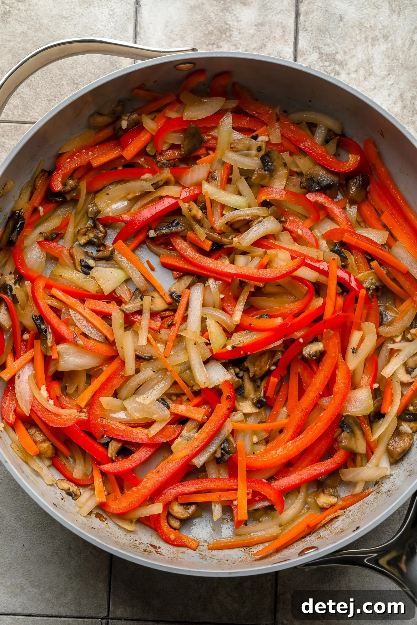 Vibrantly colored, thinly sliced vegetables like mushrooms, onions, and bell peppers cooking in a large gray skillet, creating an aromatic stir-fry base.