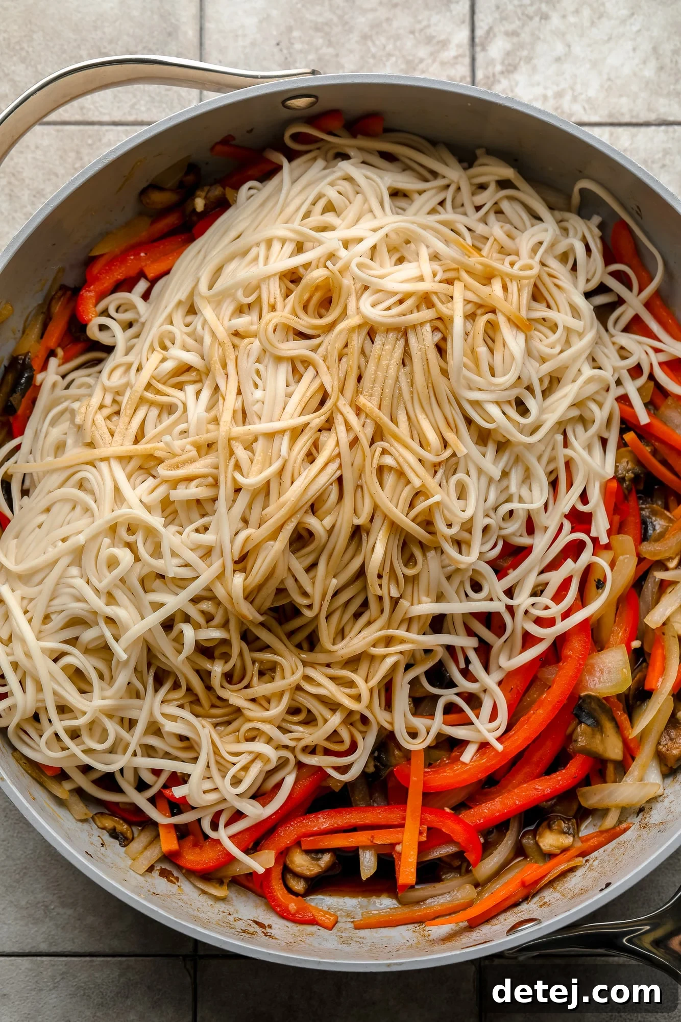 Cooked udon noodles resting on top of a colorful bed of stir-fried vegetables in a large gray skillet, ready to be tossed with sauce.