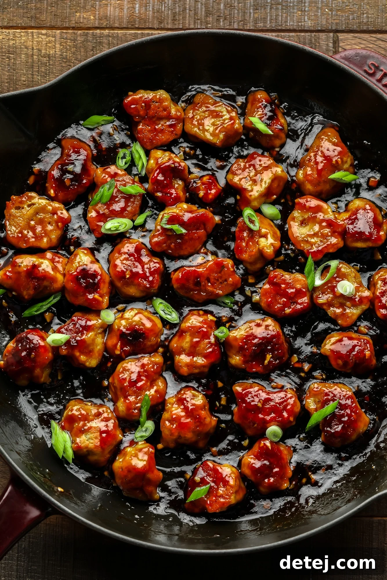 Effortless Seitan 2 close up on bite-sized seitan nuggets covered in a "honey" ginger sauce and cooking in a large black skillet.