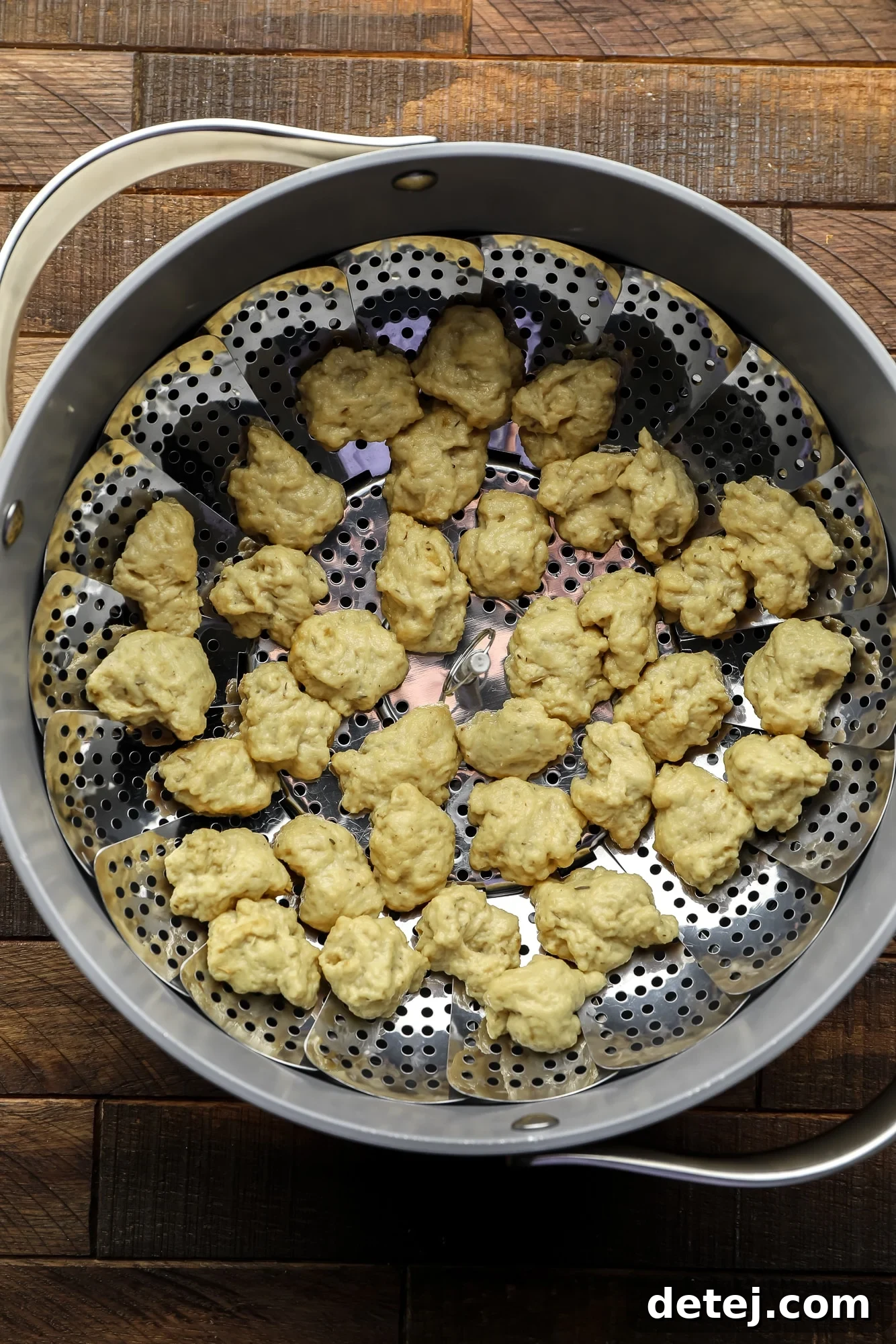 Effortless Seitan 6 raw seitan nuggets on a steamer basket in a large grey pot.