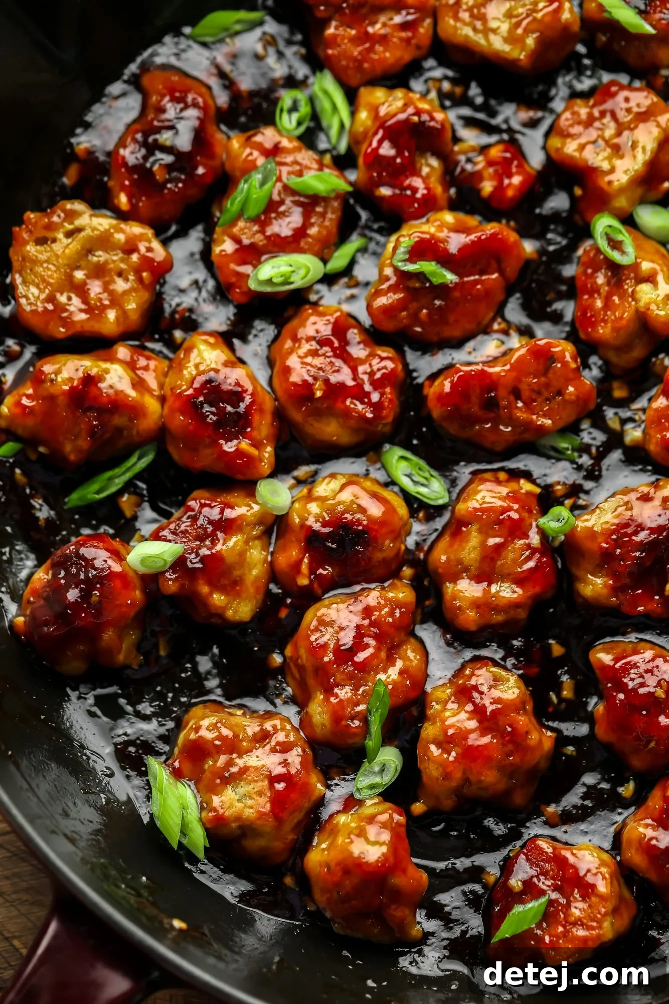 Effortless Seitan 9 close up on bite-sized seitan nuggets covered in a "honey" ginger sauce and cooking in a large black skillet.