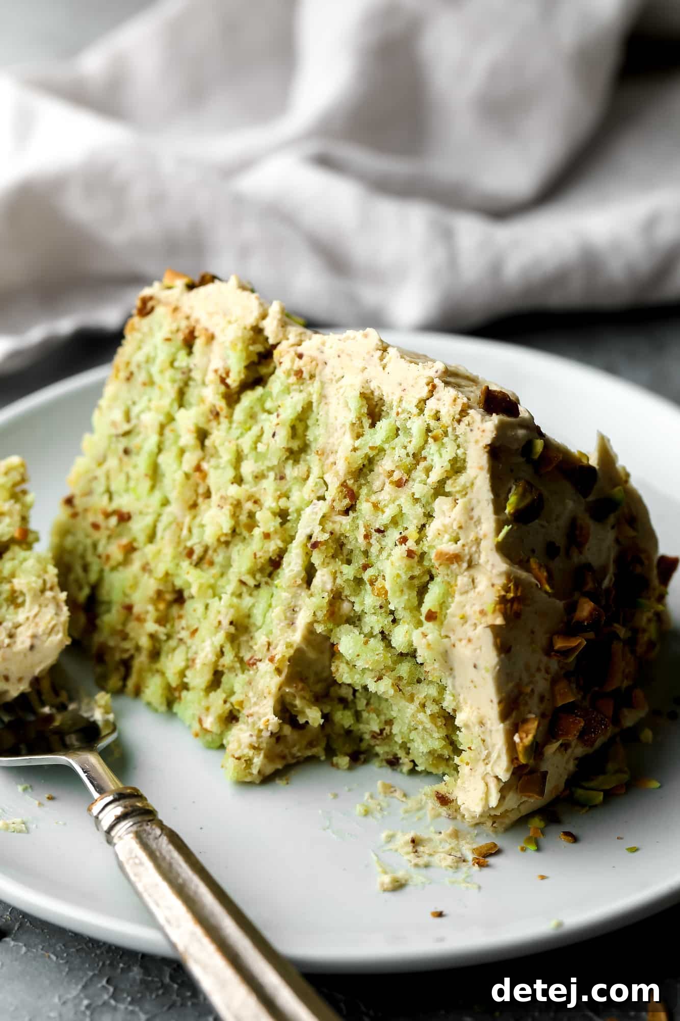 close up on a slice of vegan pistachio cake on a white plate with a bite missing.