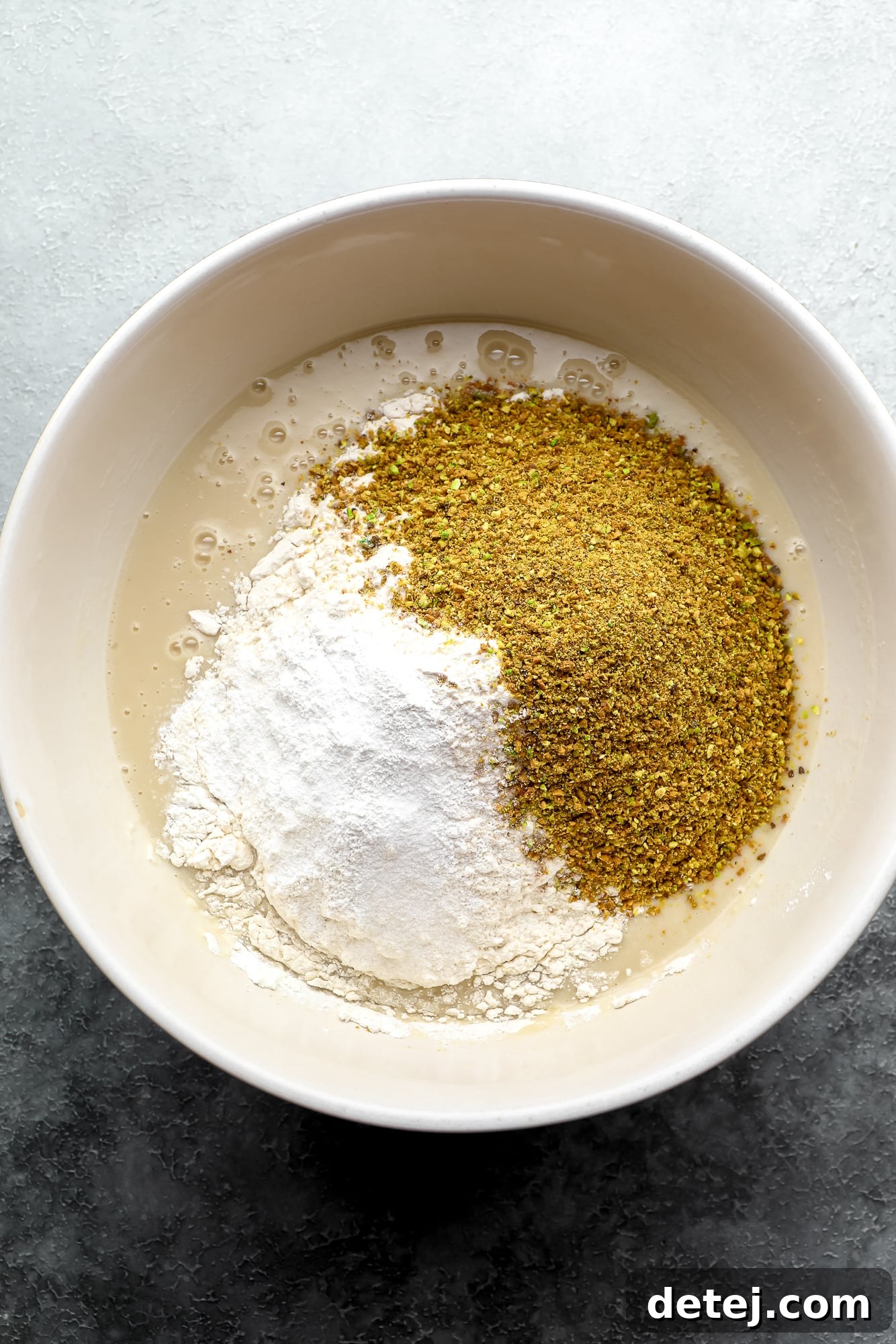 wet and dry ingredients for vegan pistachio cake in a large white bowl.
