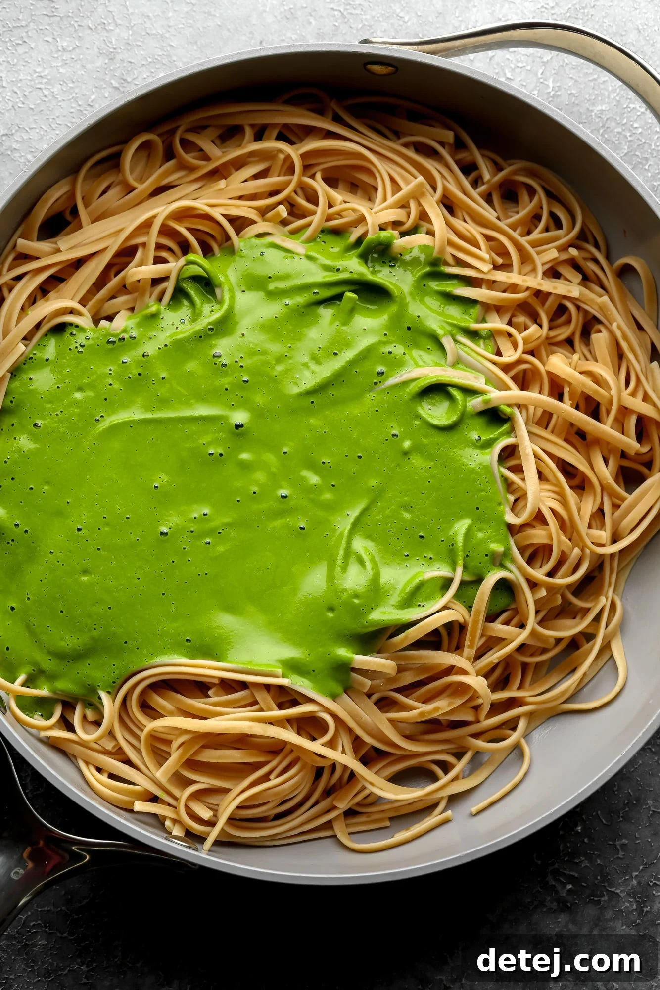 a smooth green sauce on top of cooked pasta noodles in a large grey pot.