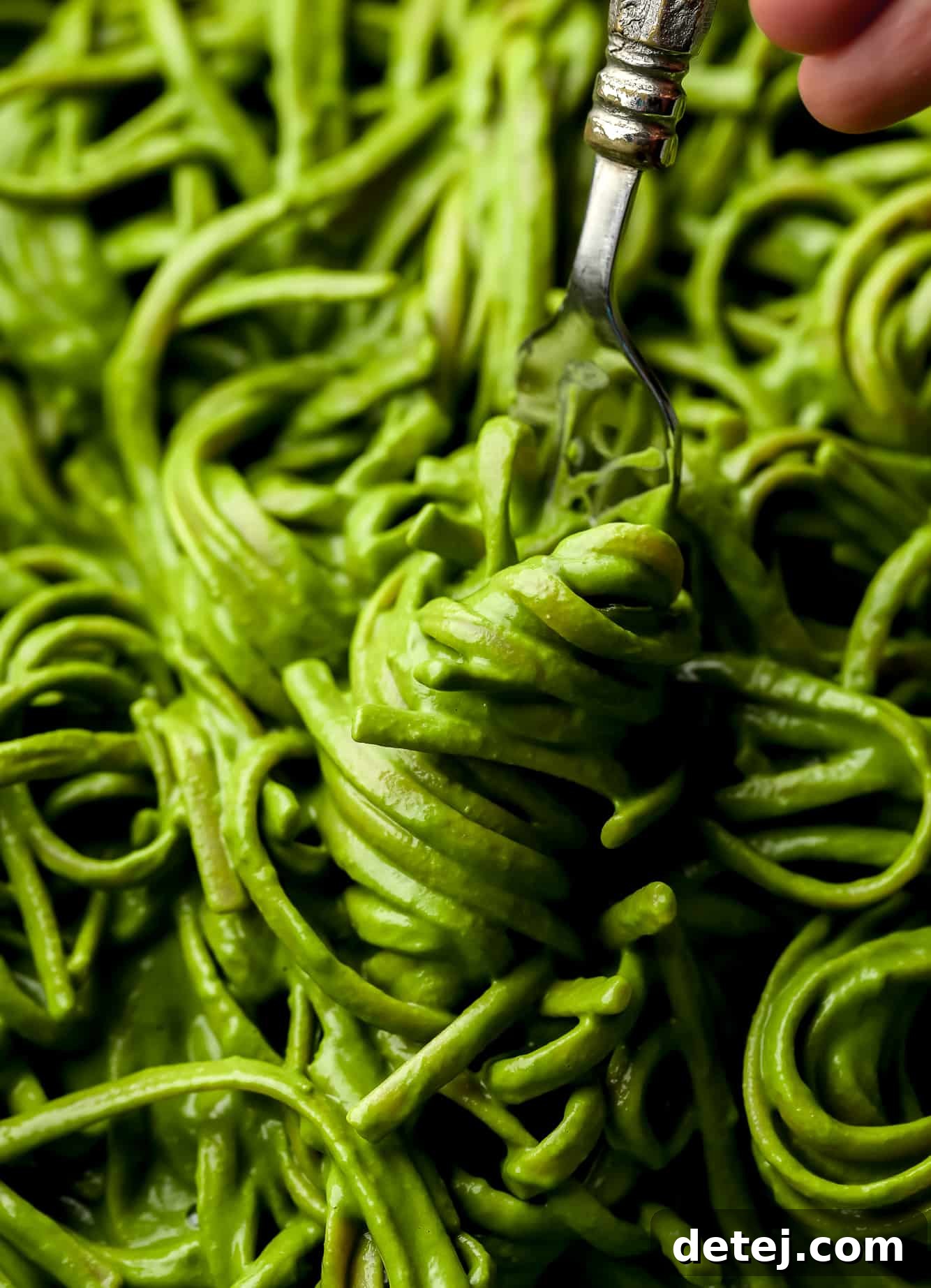 using a fork to twirl a bite of green pasta.
