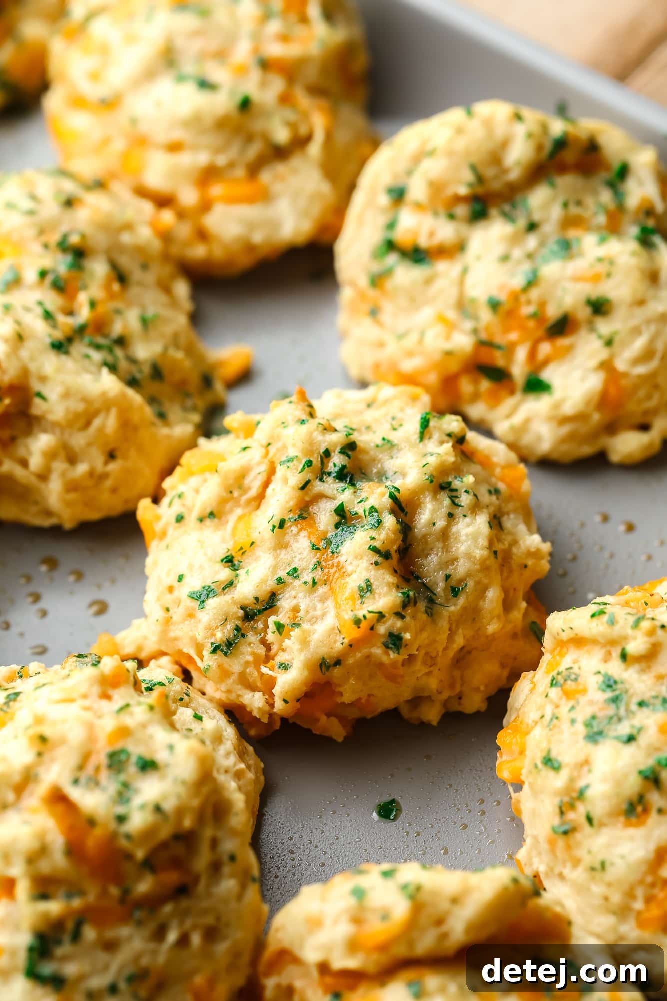 Close-up of golden brown vegan cheddar bay biscuits topped with fresh parsley on a metal baking sheet, ready to be served.