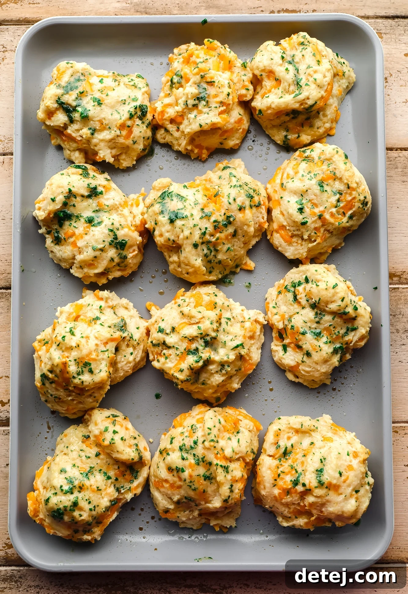 Freshly baked vegan cheddar bay biscuits, golden brown and topped with green parsley, cooling on a metal baking sheet.