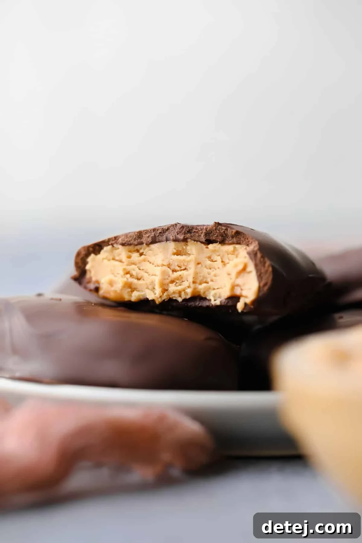 Close-up of a vegan peanut butter egg with a bite taken, showing the rich peanut butter interior, on a grey background.