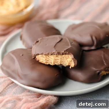 Square image of 5 peanut butter chocolate eggs, one with a bite taken out of it, on a grey plate with a pink towel.
