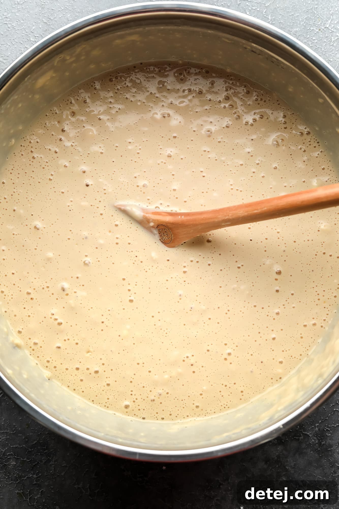 using a wooden spoon to stir vegan pancake batter in a large metal bowl.