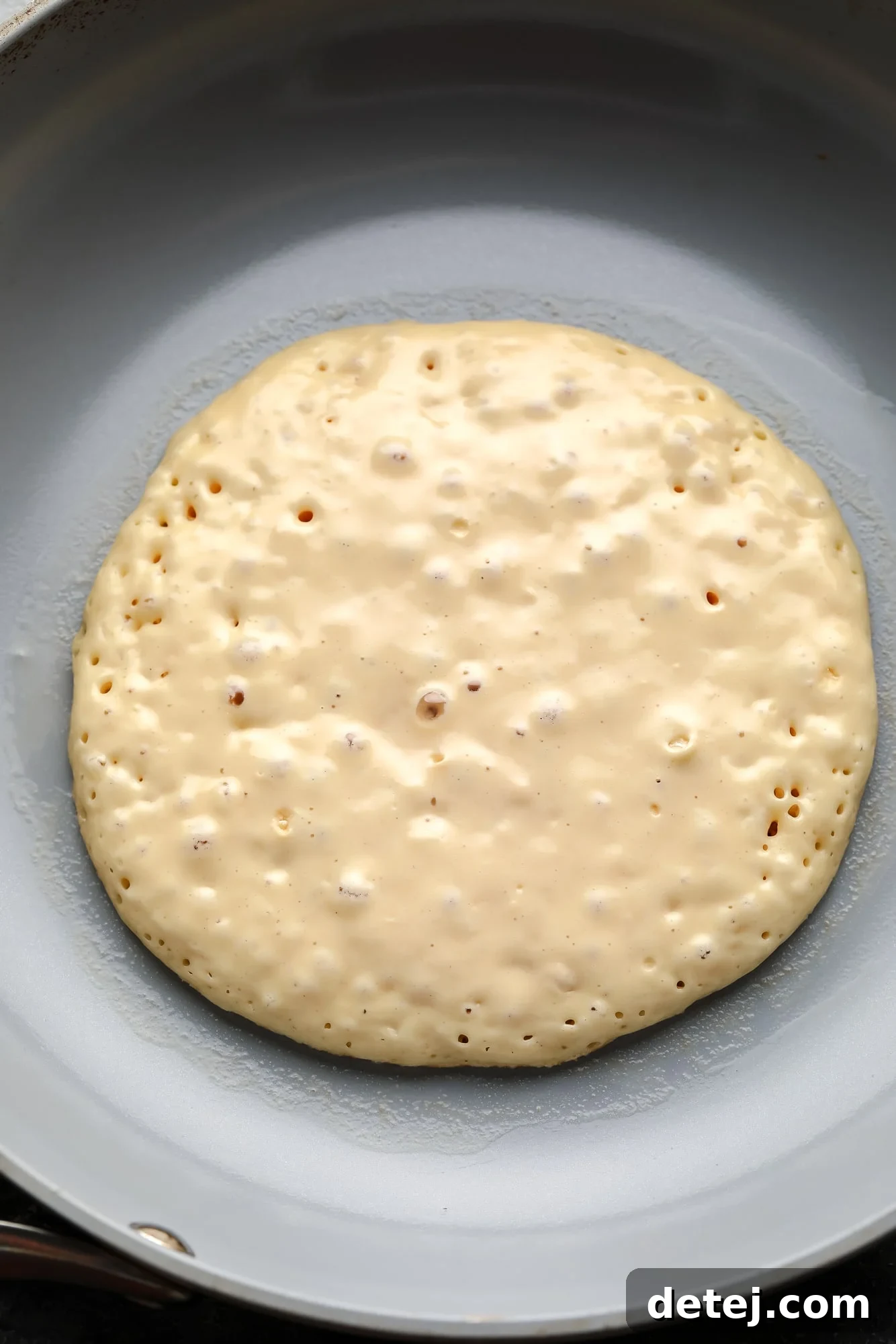cooking a vegan pancake in a grey skillet.