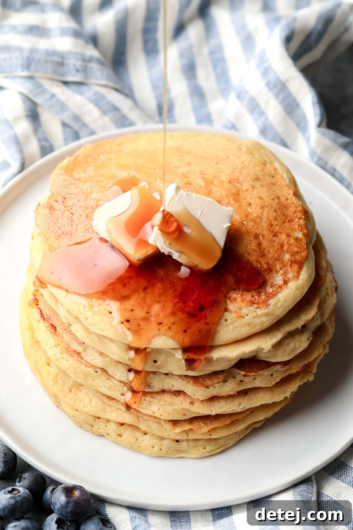 drizzling maple syrup on top of a stack of vegan protein pancakes.