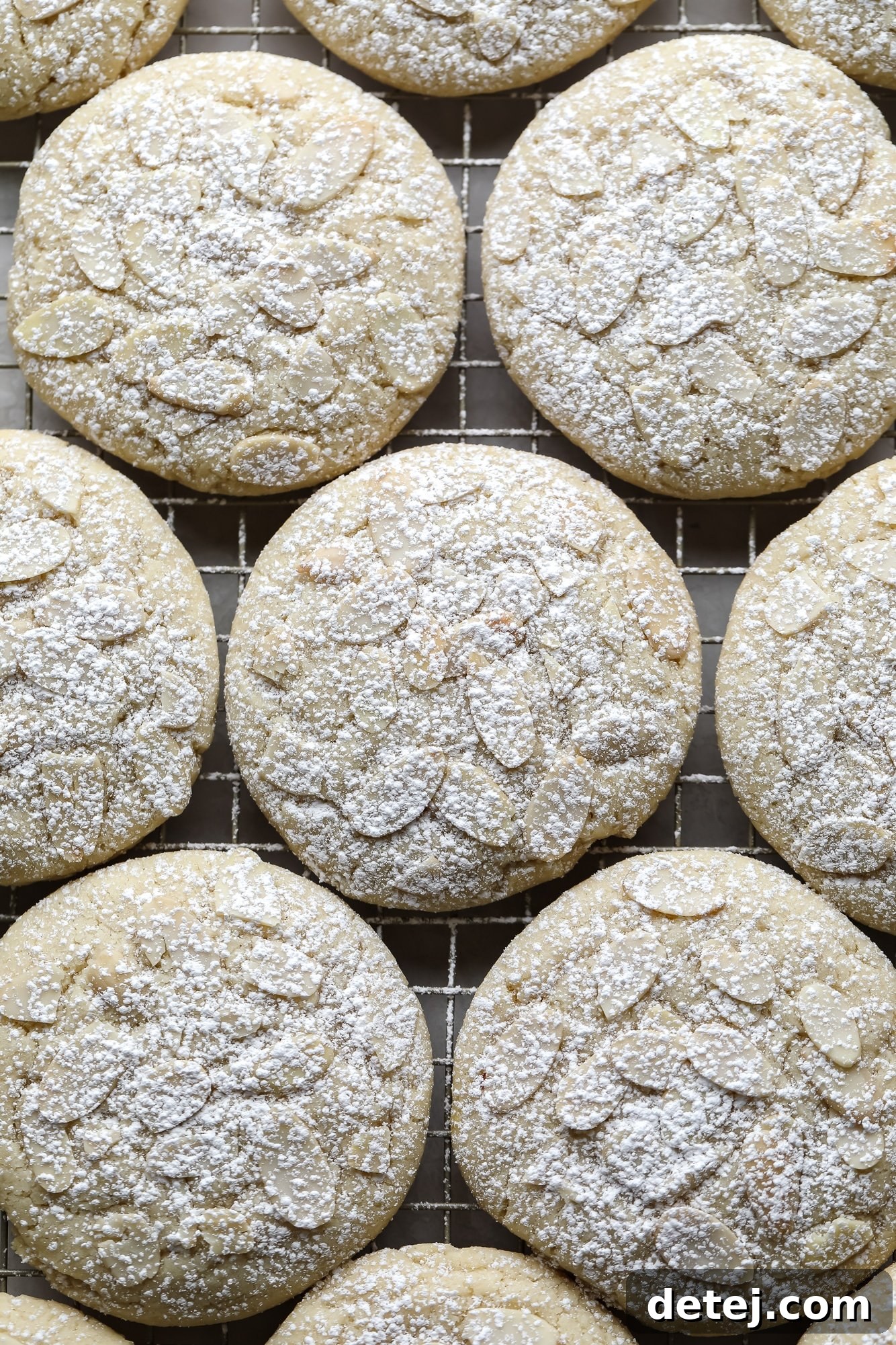 Close up on Vegan Almond Croissant Cookies topped with sliced almonds and dusted with powdered sugar, showcasing their irresistible texture and elegant presentation.