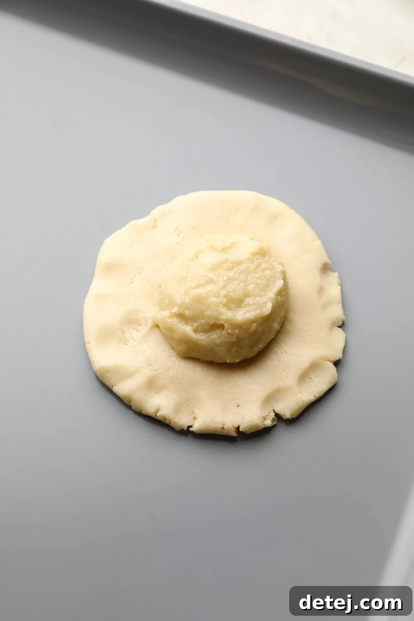 Stuffing flattened Vegan Almond Croissant Cookie dough with a scoop of creamy almond filling, preparing it for baking.