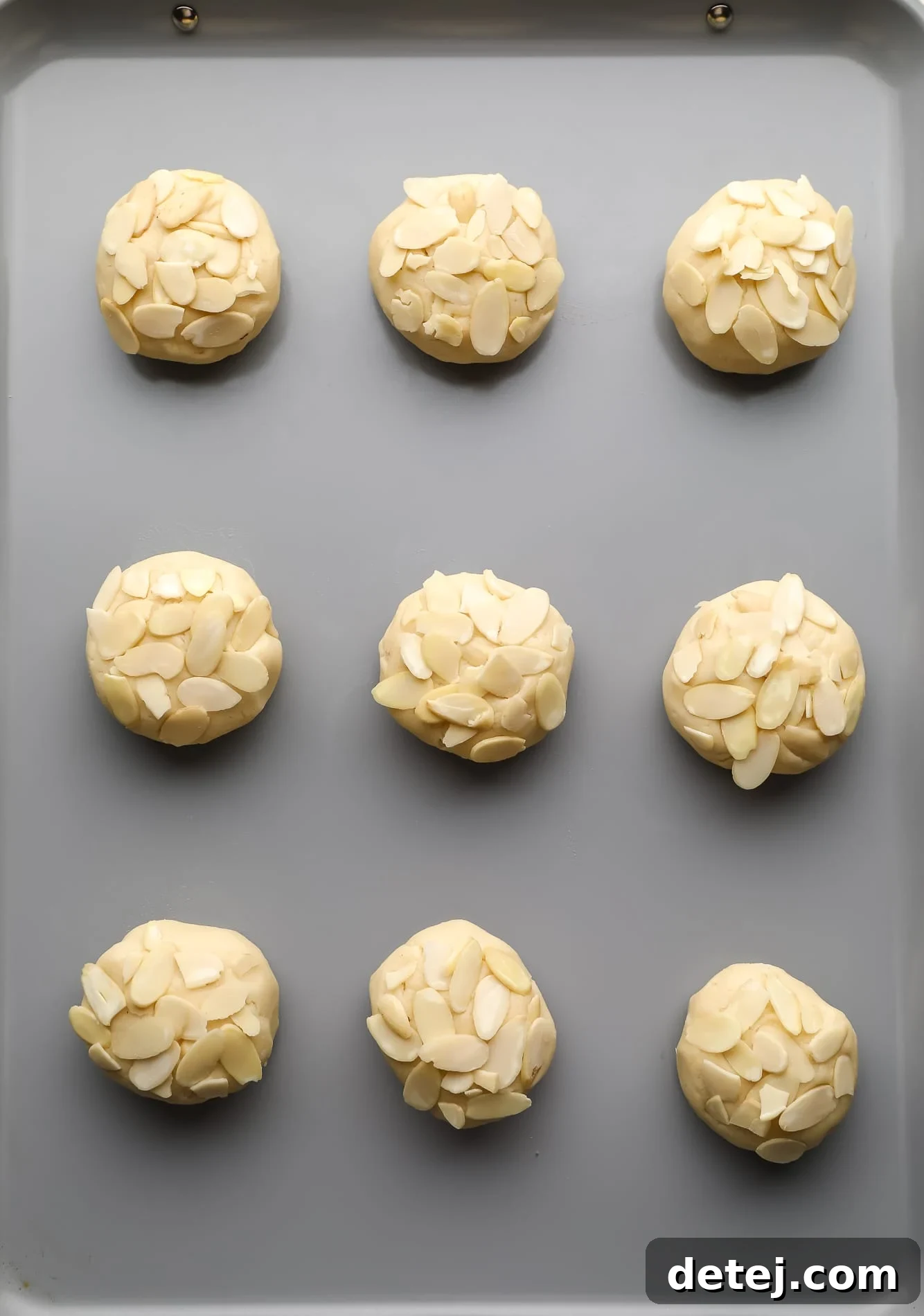 Unbaked Vegan Almond Croissant Cookies topped with sliced almonds, arranged neatly on a baking sheet before chilling and baking.