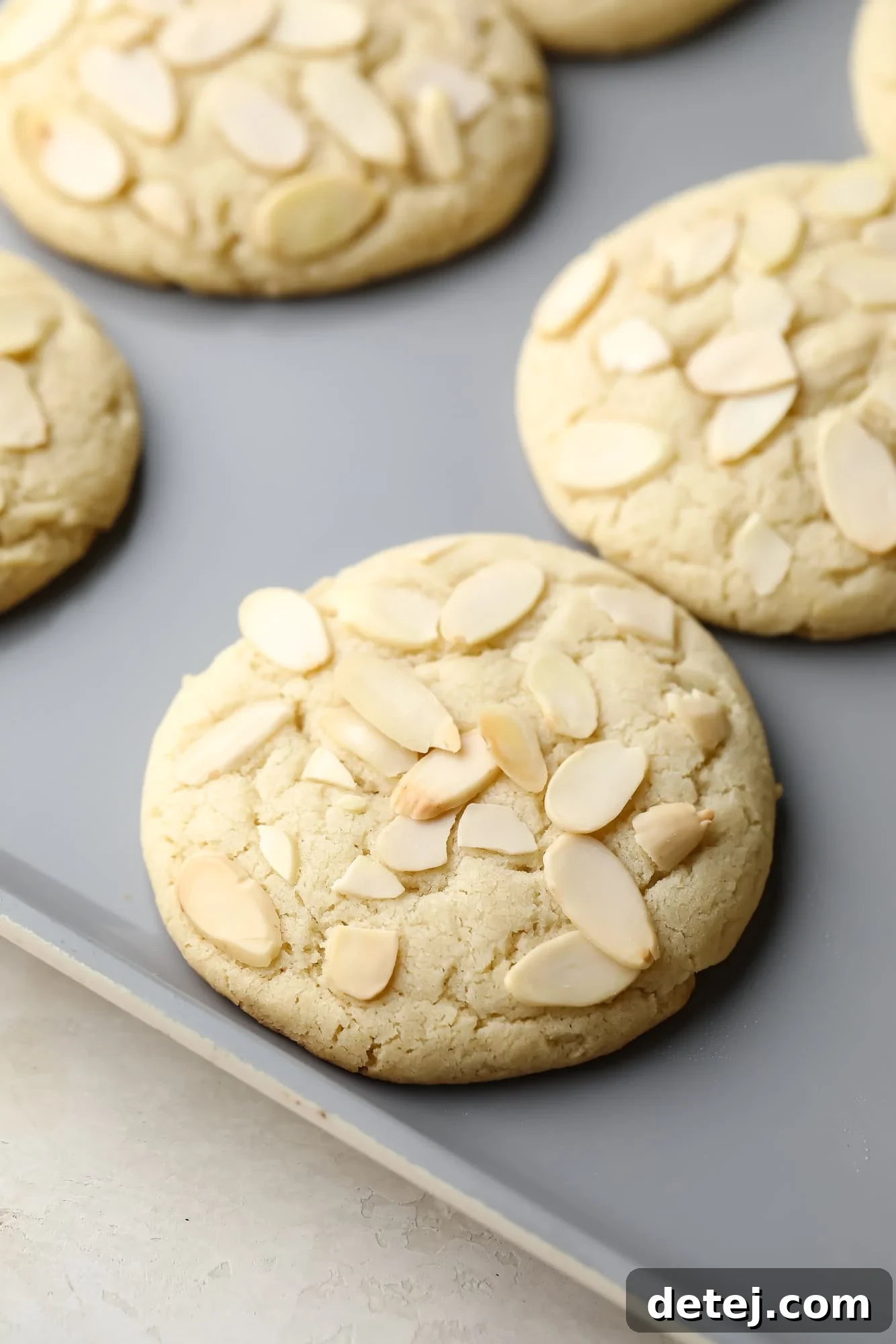 Close up on baked Vegan Almond Croissant Cookies on a baking sheet, showcasing their golden edges and delicious texture before dusting.