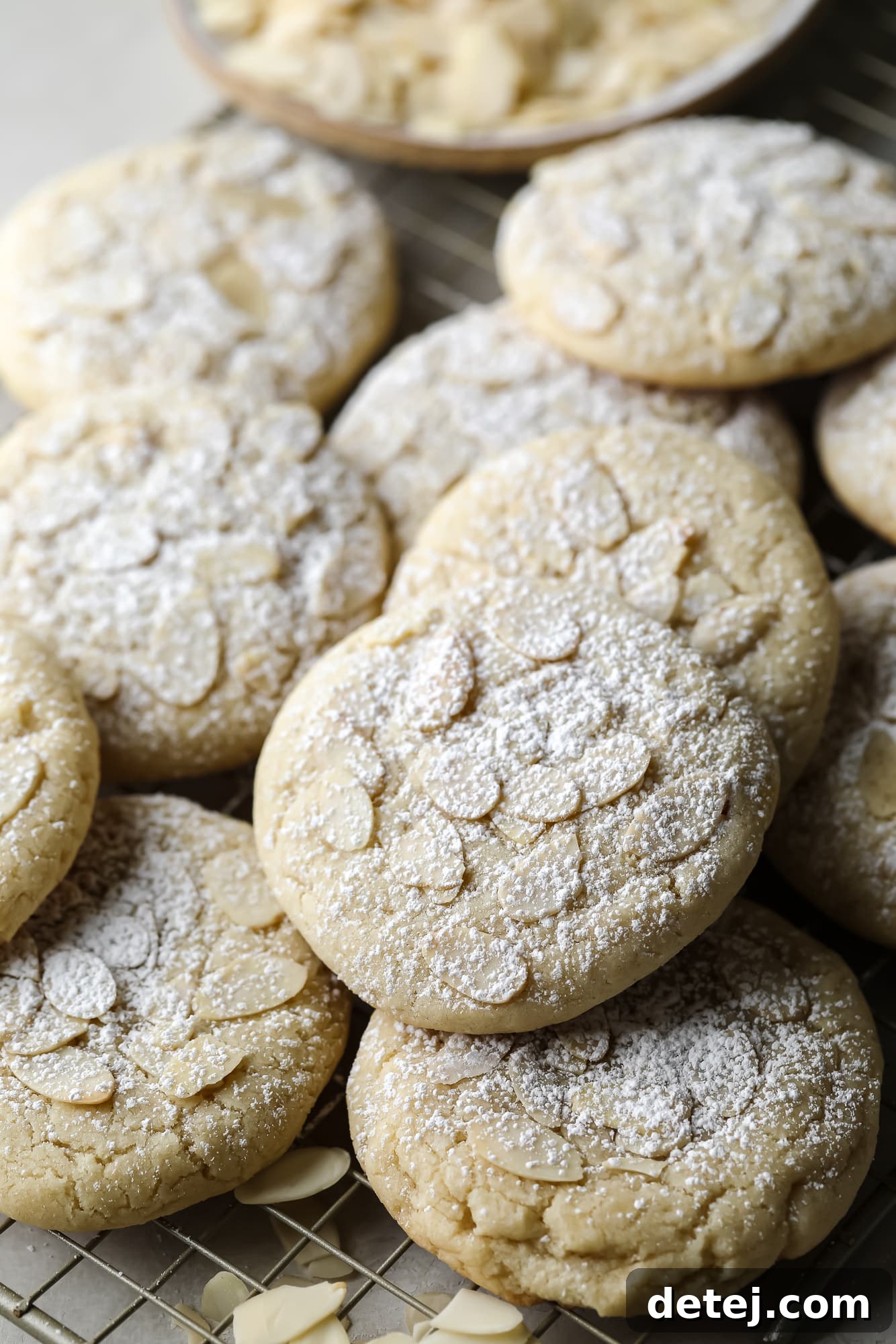 Close up on a pile of Vegan Almond Croissant Cookies topped with sliced almonds and dusted with powdered sugar, ready to be enjoyed.