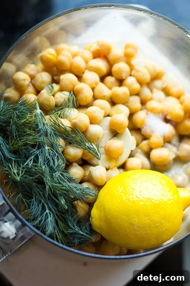 All the ingredients for lemon dill hummus, including chickpeas, fresh lemon, and a bunch of fresh dill, placed in a food processor, ready to be blended.