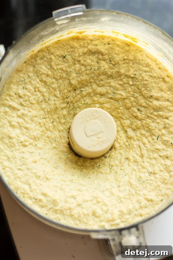 Lemon dill hummus is being blended to a smooth, creamy texture in a food processor, showing its bright yellow color.
