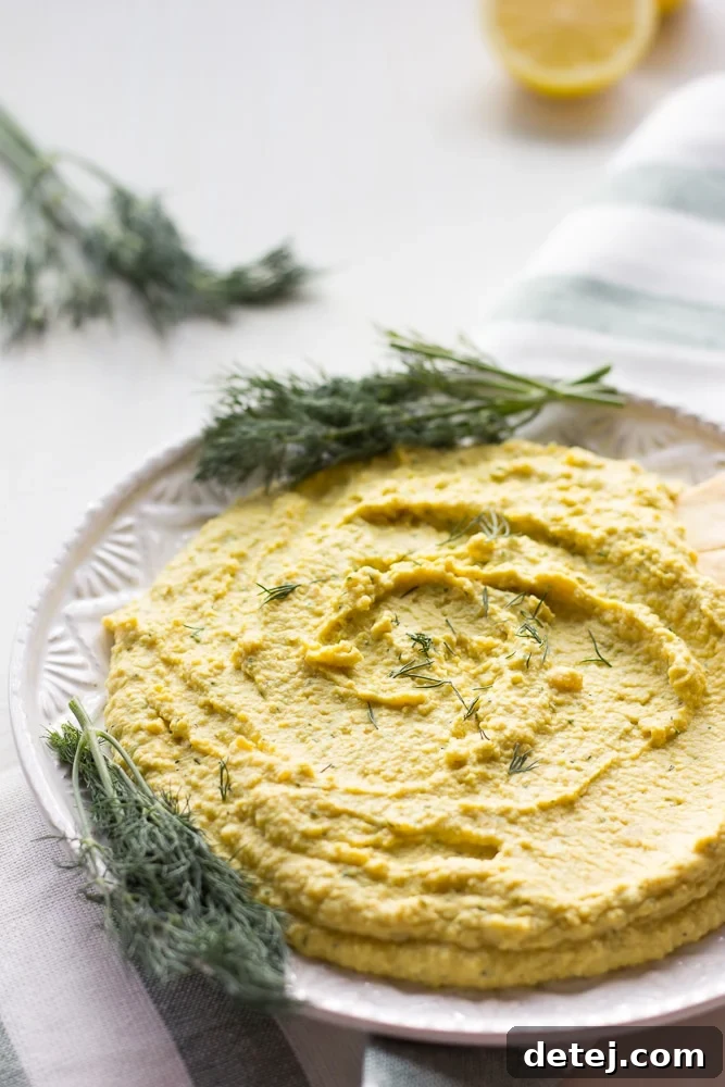 Close-up shot of creamy lemon dill hummus on a plate, garnished with fresh dill, served with crispy pita chips, photographed from a side angle.