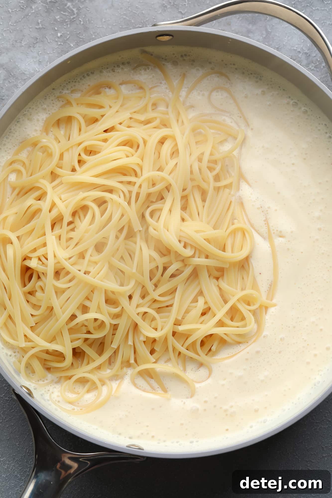 cooked pasta on top of a white, creamy sauce in a large pot.