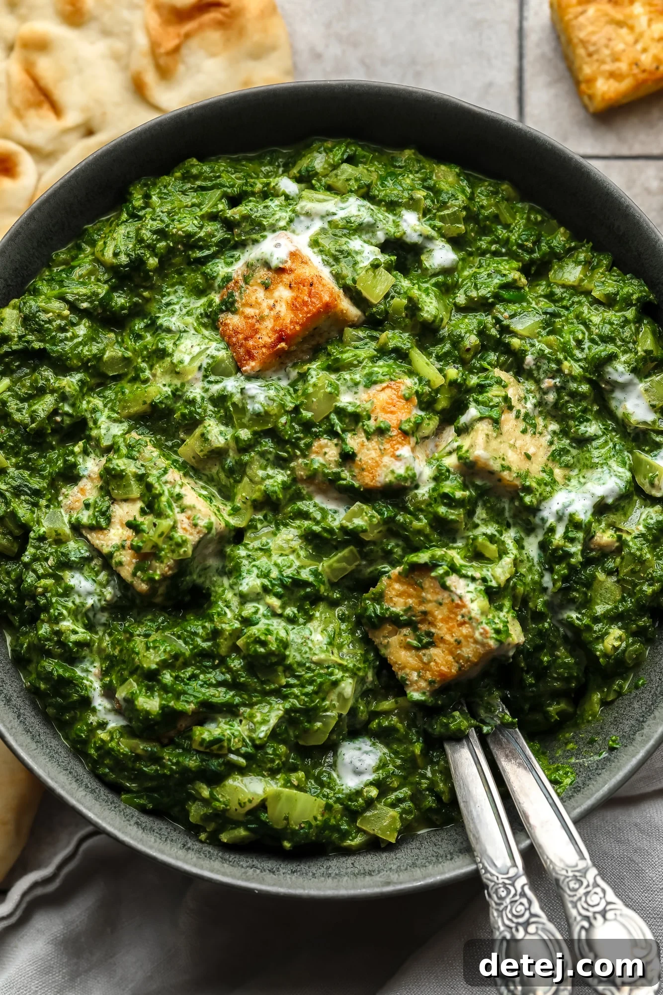 Close up on golden tofu cubes tossed in a batch of vegan palak paneer in a black bowl, garnished with fresh cilantro.