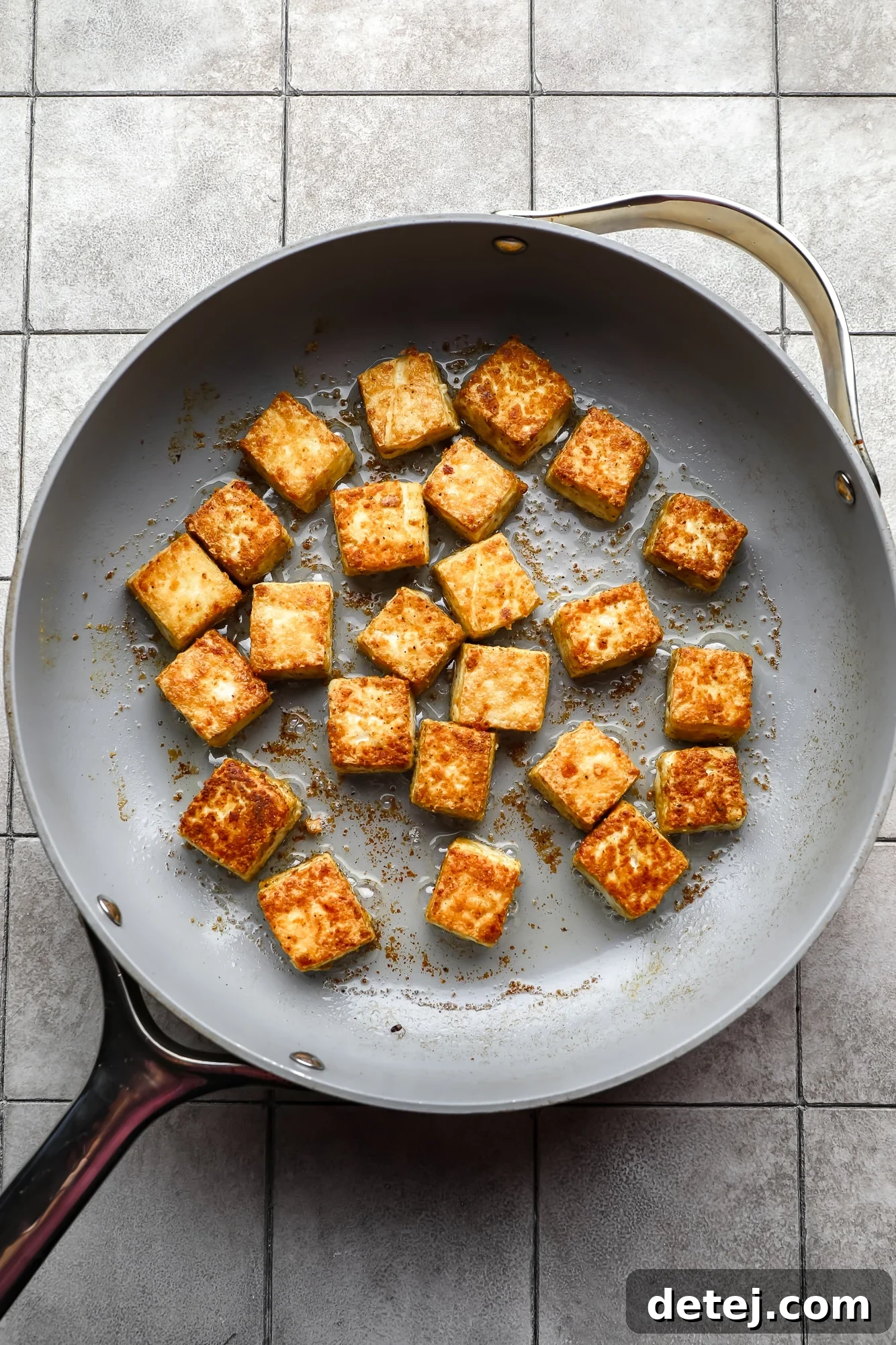 Frying seasoned tofu cubes in a large metal skillet, achieving a golden-brown crust.