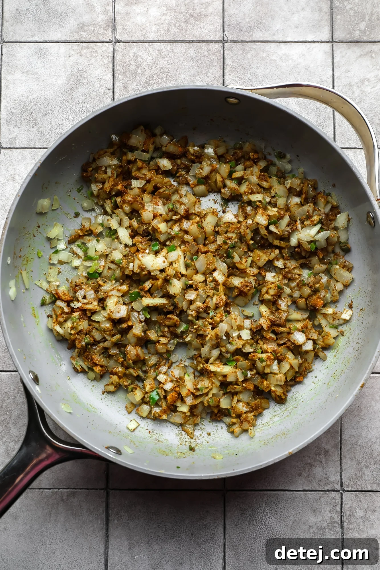 A seasoned mix of sautéed aromatics (onions, garlic, ginger, serrano pepper, cumin seeds) and ground spices in a large metal skillet.
