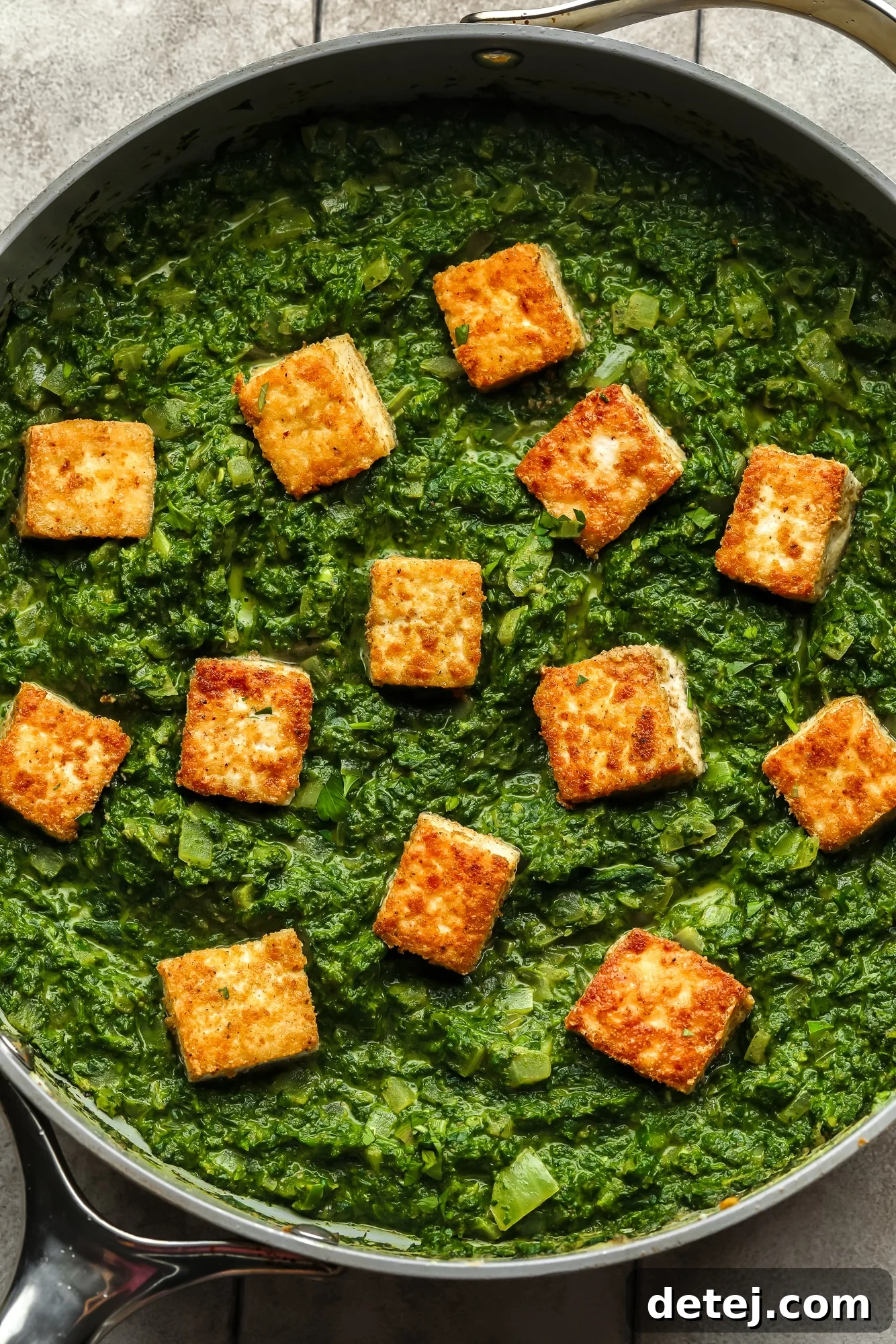 Golden tofu cubes on top of a batch of vegan palak paneer in a large skillet, ready to be served.