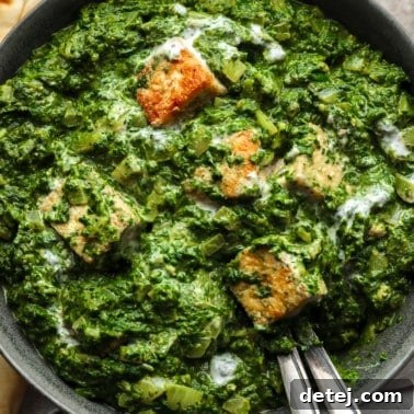Close up on golden tofu cubes tossed in a batch of vegan palak paneer in a black bowl.