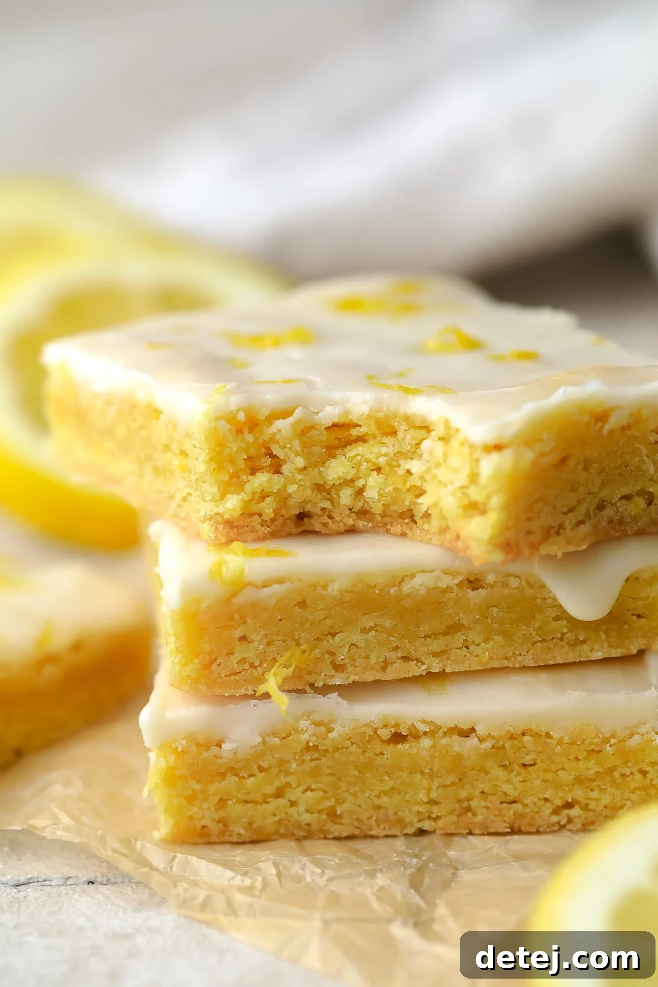 A beautifully arranged stack of golden vegan lemon brownies, topped with a delicate lemon glaze, invitingly placed on a white surface.