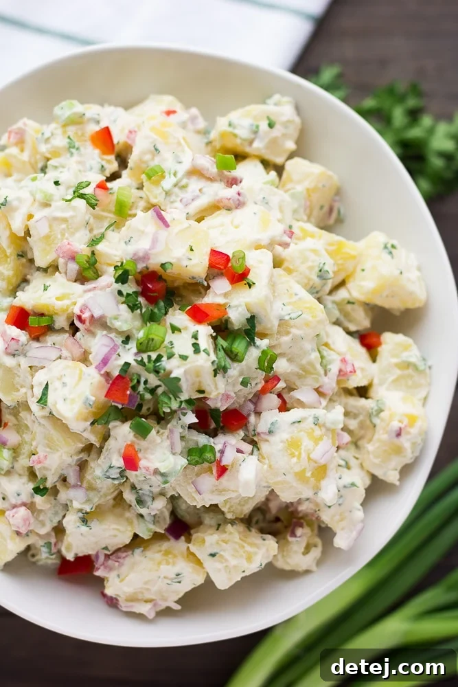 Close up of healthy vegan potato salad in a white bowl, showing creamy texture and colorful vegetables.