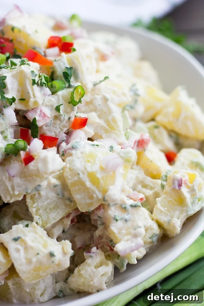 Side view of vegan potato salad in a white bowl, garnished with fresh herbs.