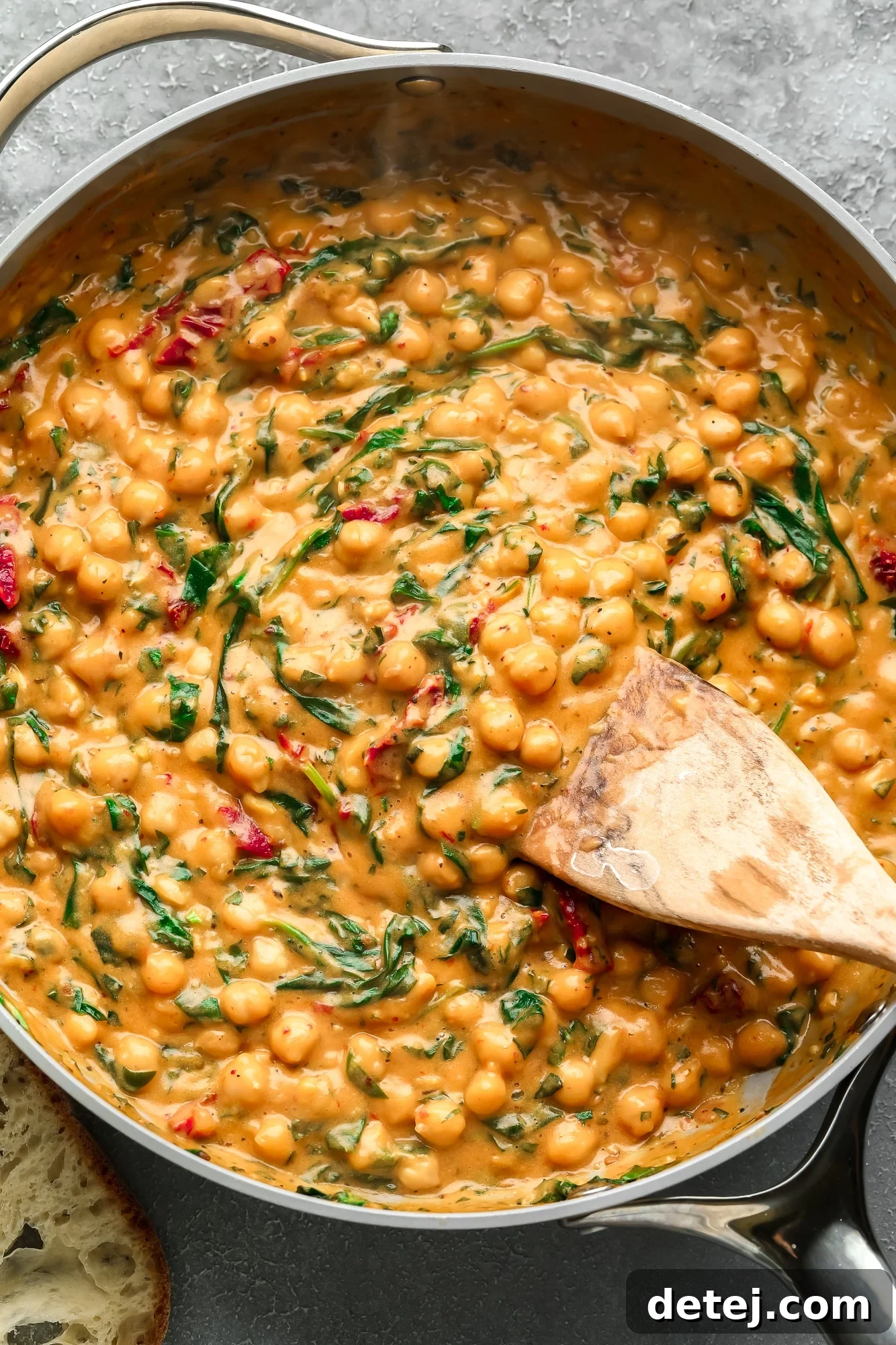 The Chickpea Proposal 2 a wooden spoon stirring a batch of Marry Me Chickpeas in a large skillet.