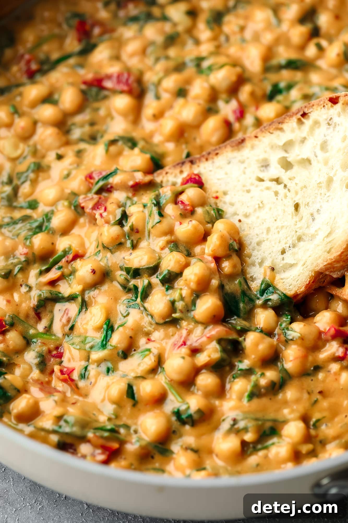 The Chickpea Proposal 5 using a piece of bread to scoop up a bite of Marry Me Chickpeas from a skillet.