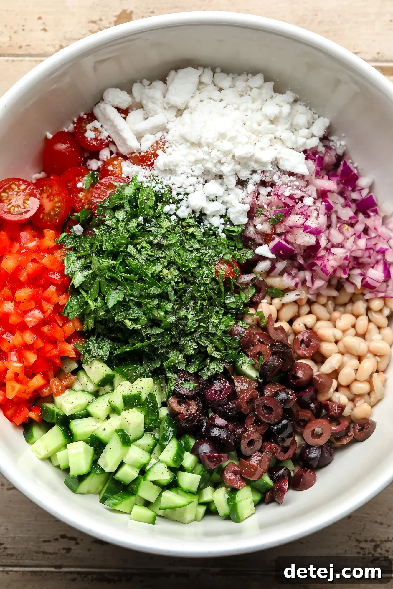 All the fresh ingredients for a Mediterranean white bean salad laid out in a large white bowl before mixing.
