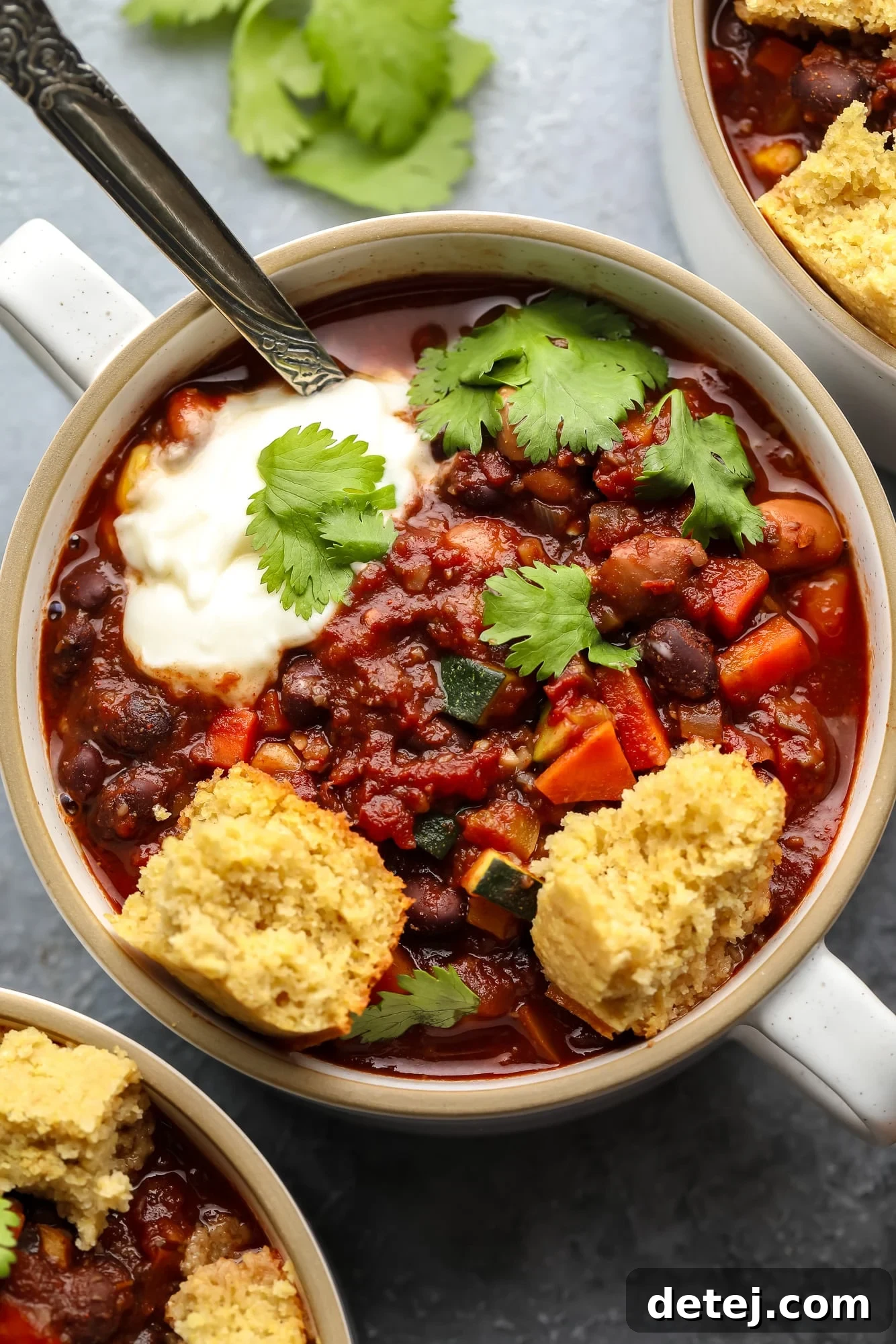 A small bowl of hearty veggie chili topped with crumbled vegan cornbread and fresh cilantro.
