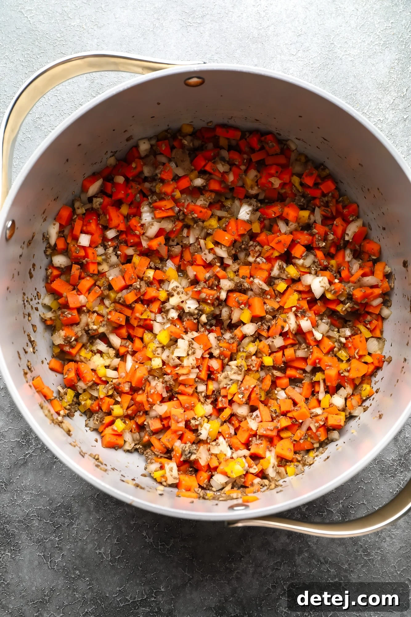 A close-up view of a colorful medley of chopped vegetables, including mushrooms, onions, carrots, and bell peppers, sautéing in a large pot.