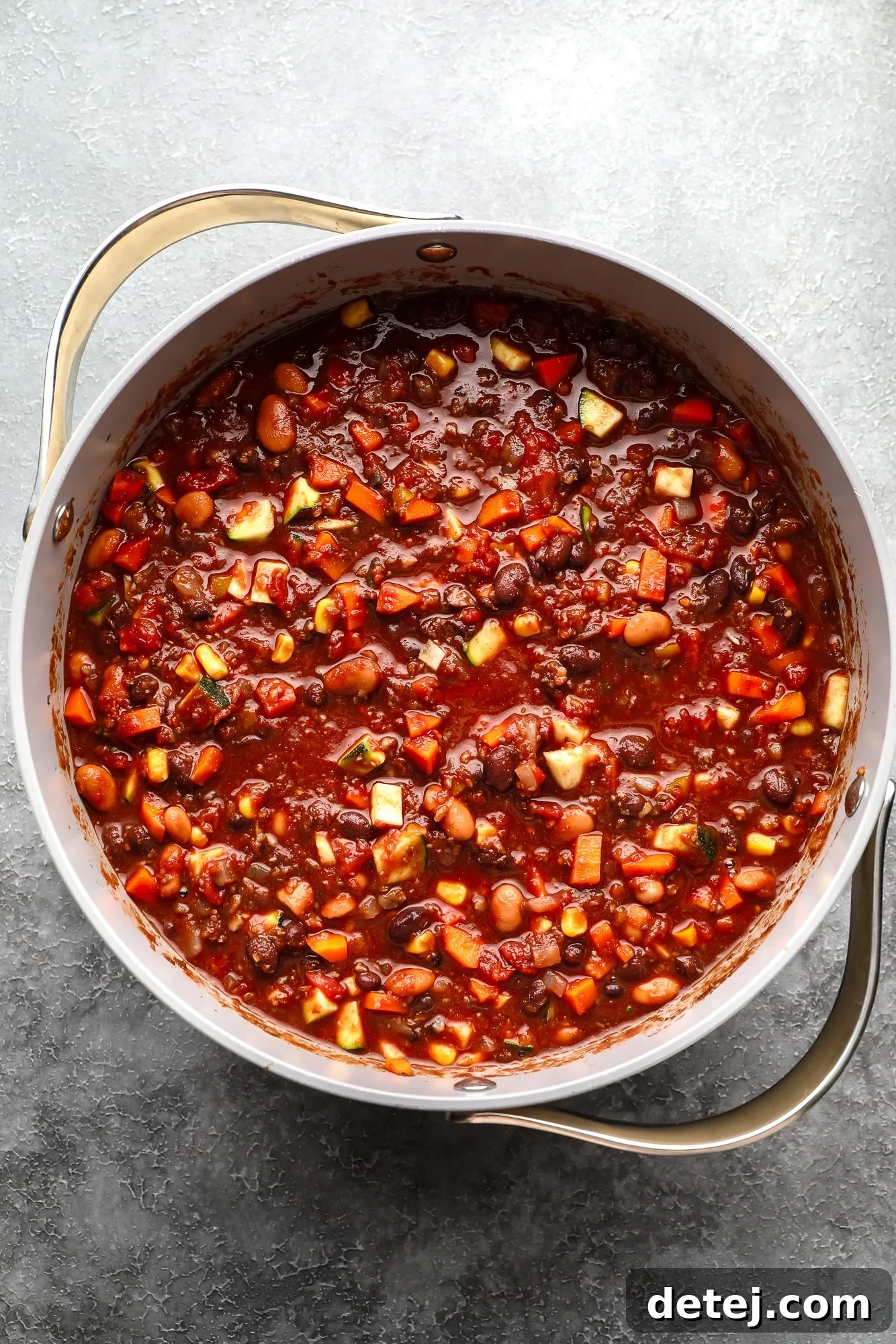 A close-up shot of rich, simmering veggie chili in a large pot, with steam rising and vibrant ingredients visible.