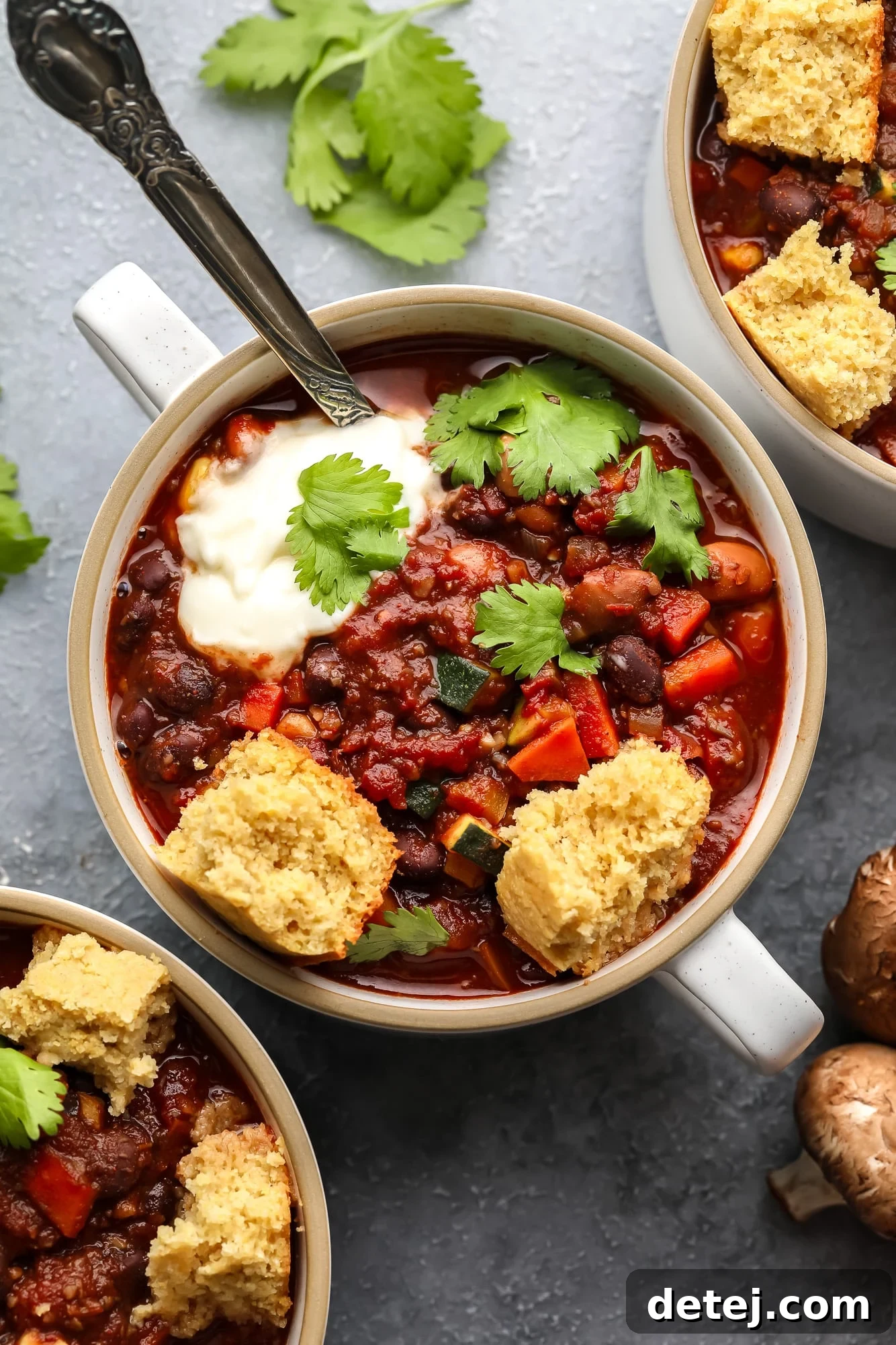 A small, rustic bowl filled with vibrant veggie chili, garnished with a sprinkle of fresh green herbs and a side of golden vegan cornbread.