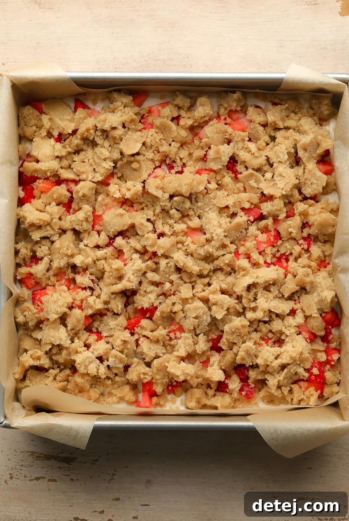 An unbaked batch of Vegan Strawberry Cheesecake Crumble Bars neatly arranged in a square baking tin, ready for the oven.
