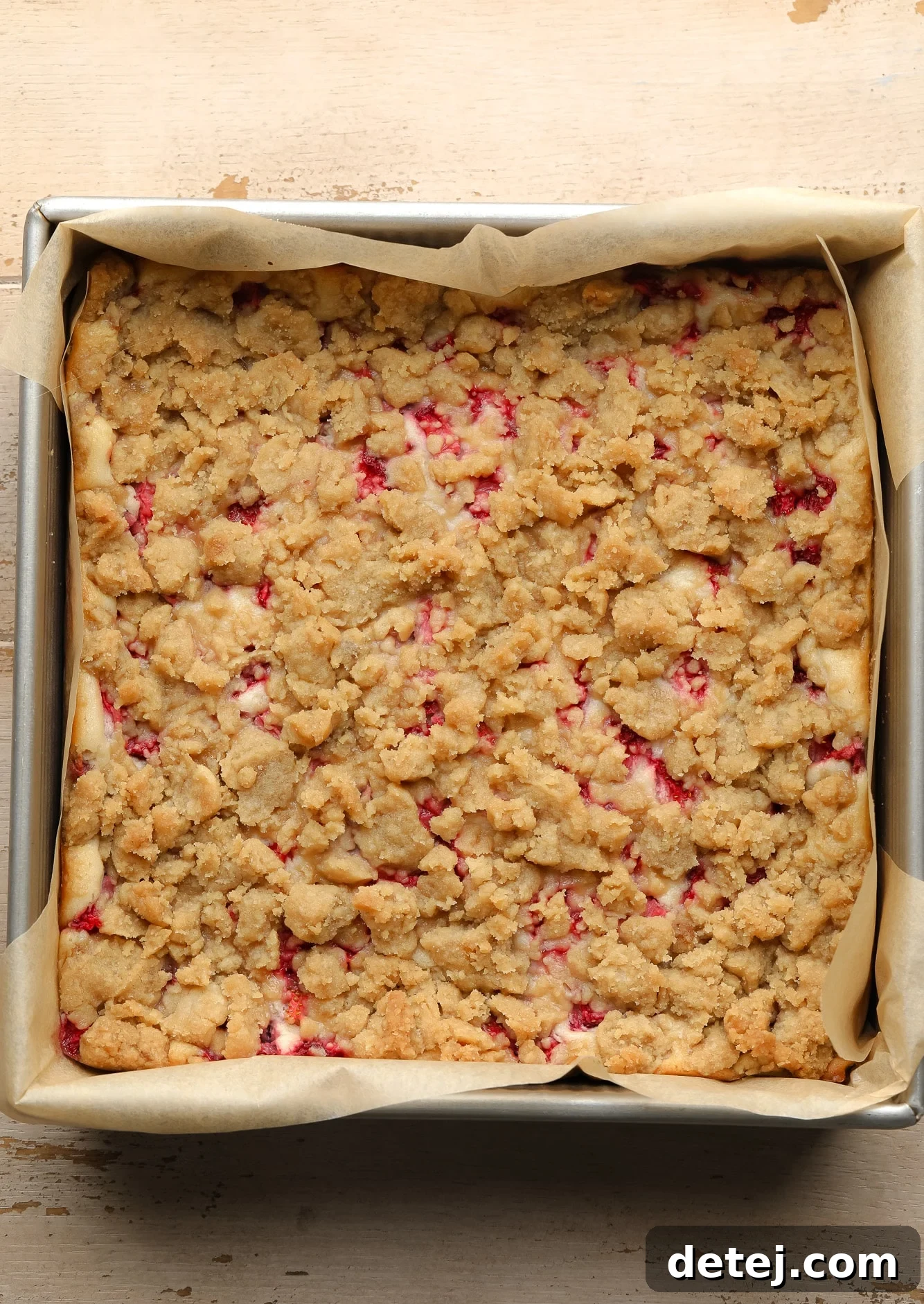 An baked batch of golden Vegan Strawberry Cheesecake Crumble Bars still warm in a square baking tin, ready for cooling.